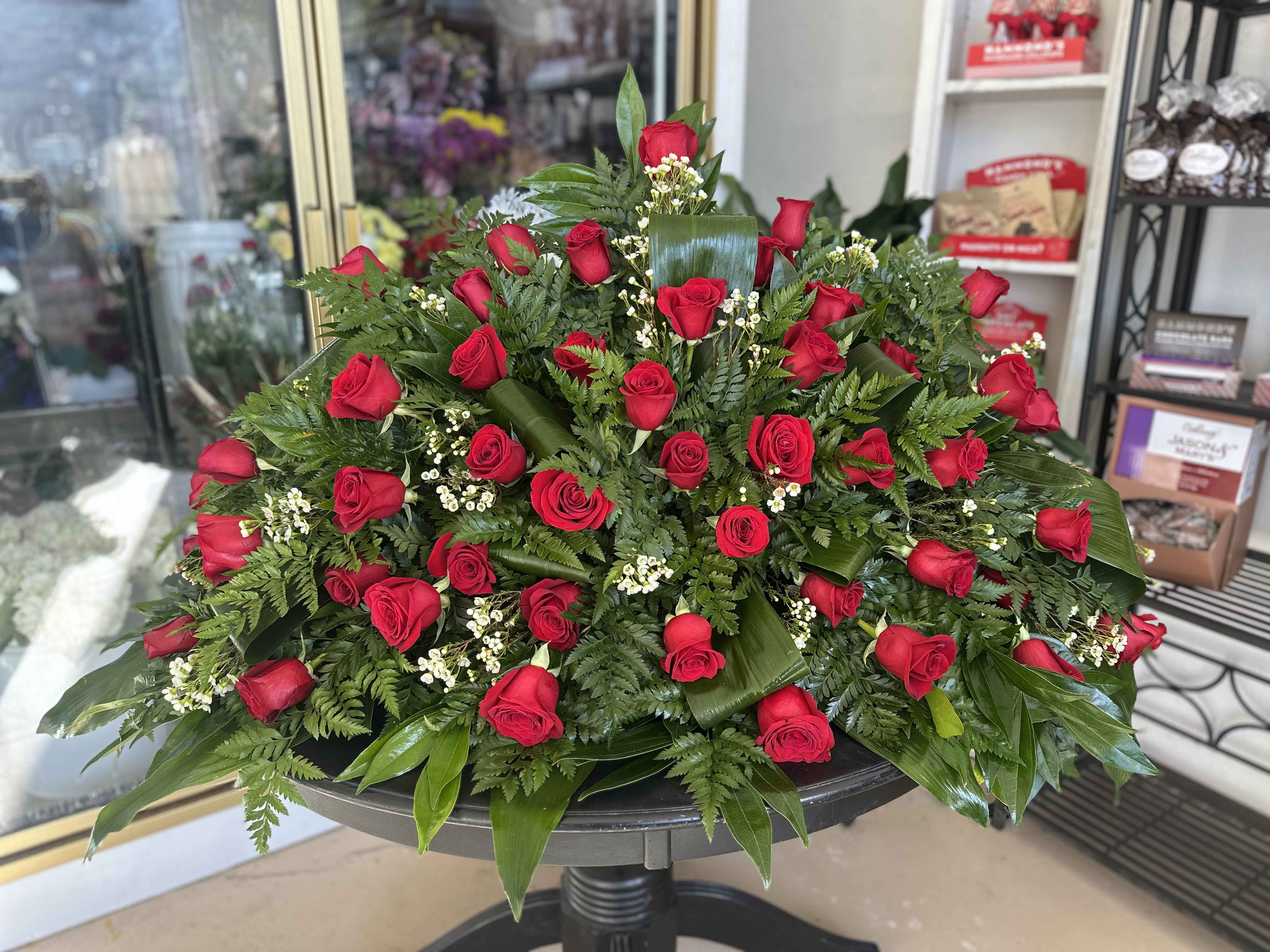 Red Rose Casket Spray - An abundance of red roses will express your love and devotion with beauty. This classic casket spray of roses mixed with greenery will be a fragrant reminder on a solemn day. (Photo shown is premium selection)