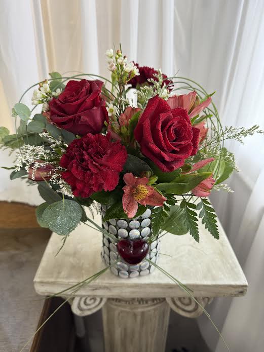 Tried and True (Is My Love for You) - Two red roses and accent flowers are wrapped in a bear grass heart.  Another red glass heart adorns the front of the vase.