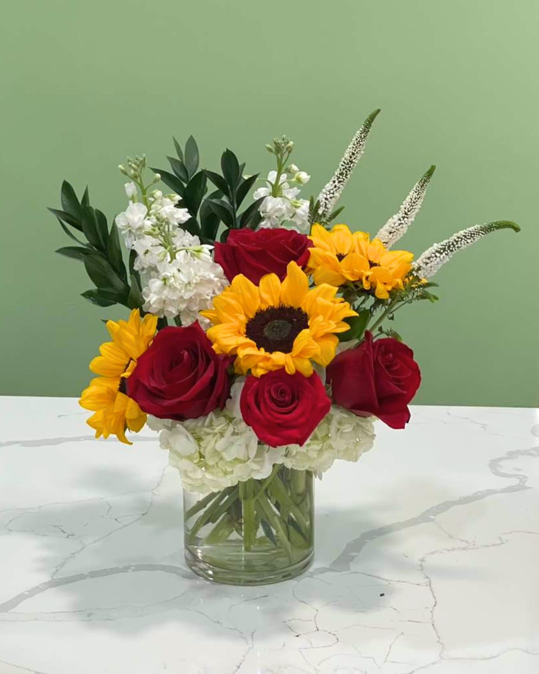 Today &amp; Forevermore - This joyful arrangement has bright sunflowers, rich red roses, soft white stock, fluffy white hydrangeas, dainty white veronicas and green ruscus in a clear cylinder vase. 