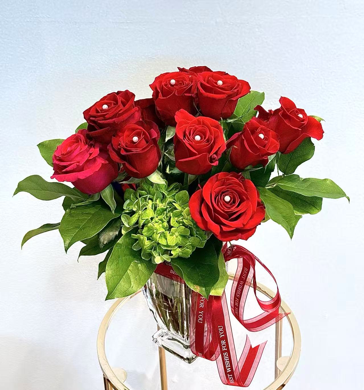 Eternal Red by Tiffany's Blooms - A timeless vase arrangement featuring premium red roses accented with fresh greenery and a touch of green hydrangea for balance and texture. Finished with elegant pearl details, this design is romantic, refined, and ready to display. A perfect choice for anniversaries, love celebrations, and meaningful gifts.