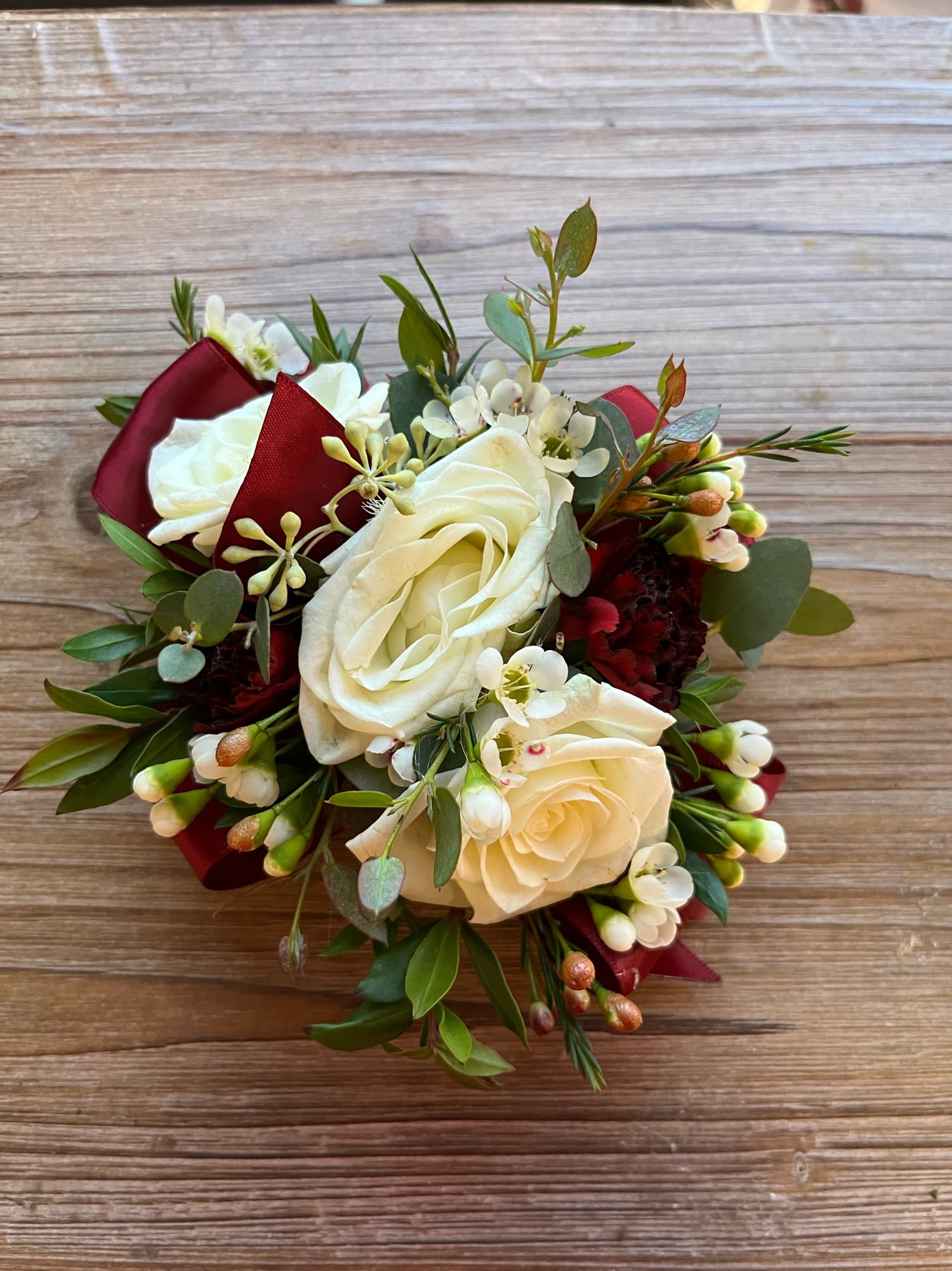 Wrist Corsage #7 Roses and Carnations - White spray roses, burgundy pixie carnations, variety of greenery and filler. Please specify ribbon color