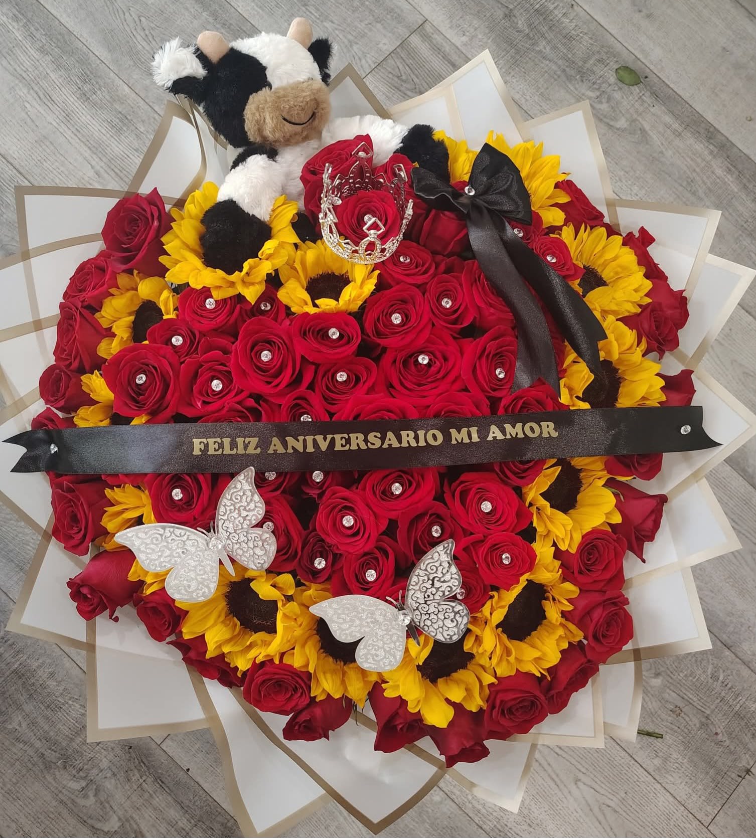 Vaquero bouquet - A bouquet of sunflowers with a plush cow, red roses, and more sunflowers. It's heart-shaped, an elegant and very large bouquet. Ribbon  personalized  snd crown 