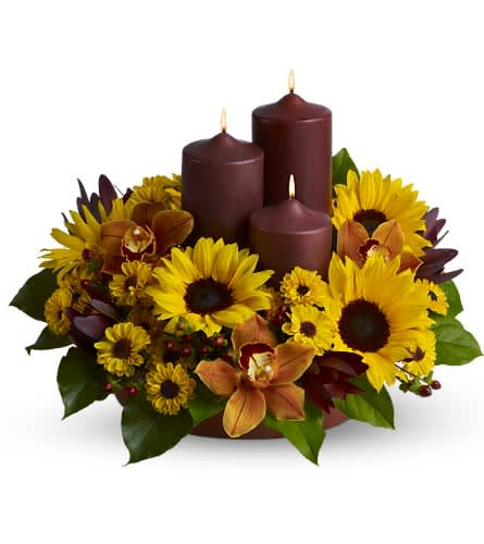 Rustic Radiance  - This rustic display of three chocolate-colored pillar candles surrounded by bright sunflowers, orchids and more, in glowing tones of yellow and bronze, makes a delightful centerpiece for a Thanksgiving feast or fall dinner party, and is also a lovely decorative accent for an entryway.    A mix of fresh flowers such as sunflowers, Viking spray chrysanthemums, cymbidium orchids and more, in shades of yellow and bronze - accented with preserved oak leaves - are arranged in a tray with three chocolate-colored pillar candles of different heights.    Approximately 18" (W) x 13" (H)    Orientation: All-Around        As Shown : TFWEB459    
