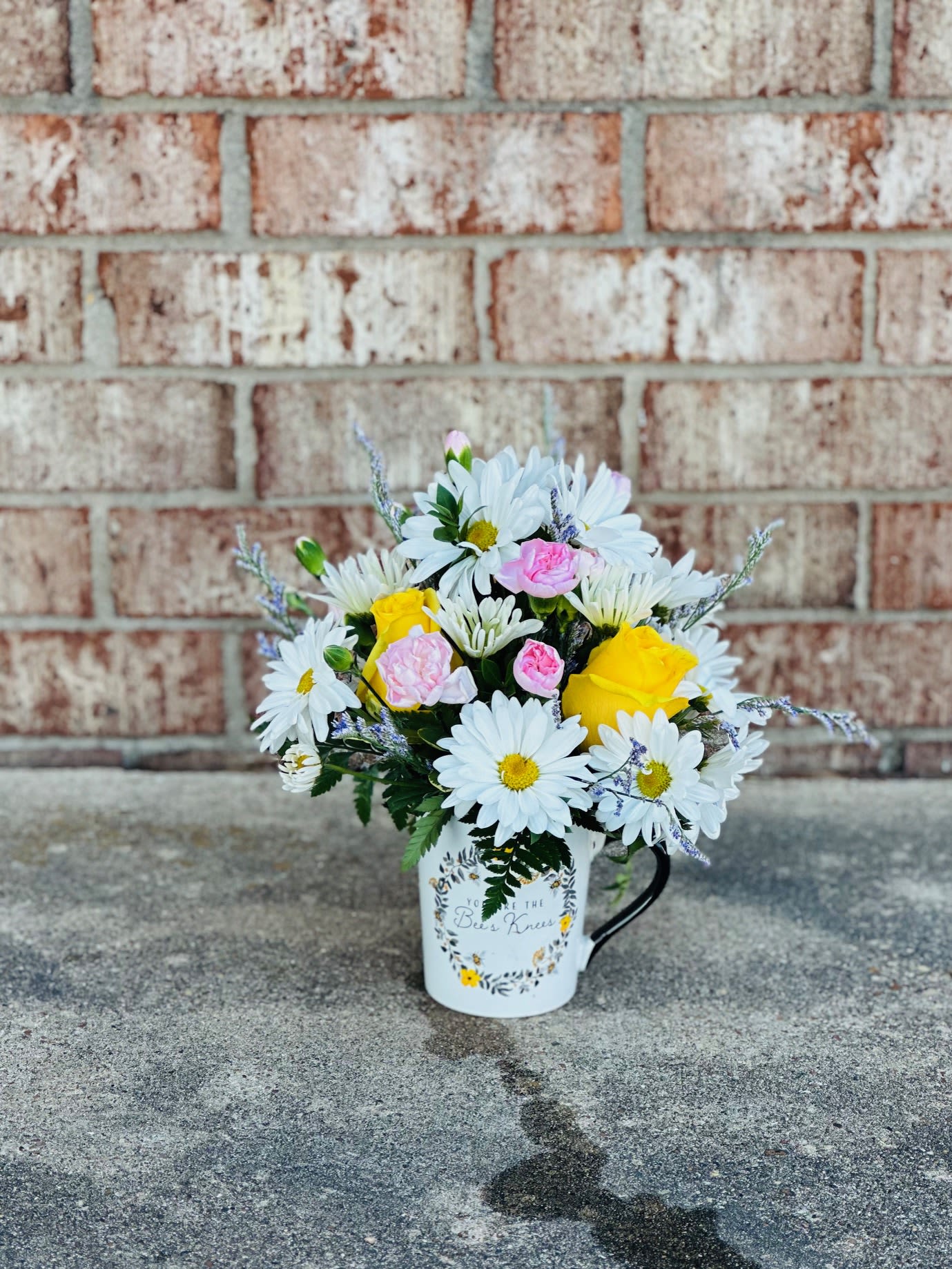 You’re the Bee’s Knees - Bright, happy, and full of charm, You’re the Bee’s Knees is a Valentine’s arrangement that celebrates love in its most joyful form. Designed in a keepsake “You’re the Bee’s Knees” mug, this sweet arrangement features sunny yellow roses, crisp white daisies, soft pink mini carnations, and a touch of blue misty for a fresh pop of color.  Perfect for Valentine’s Day when you want something fun, thoughtful, and guaranteed to make them smile—because some loves are just the bee’s knees.