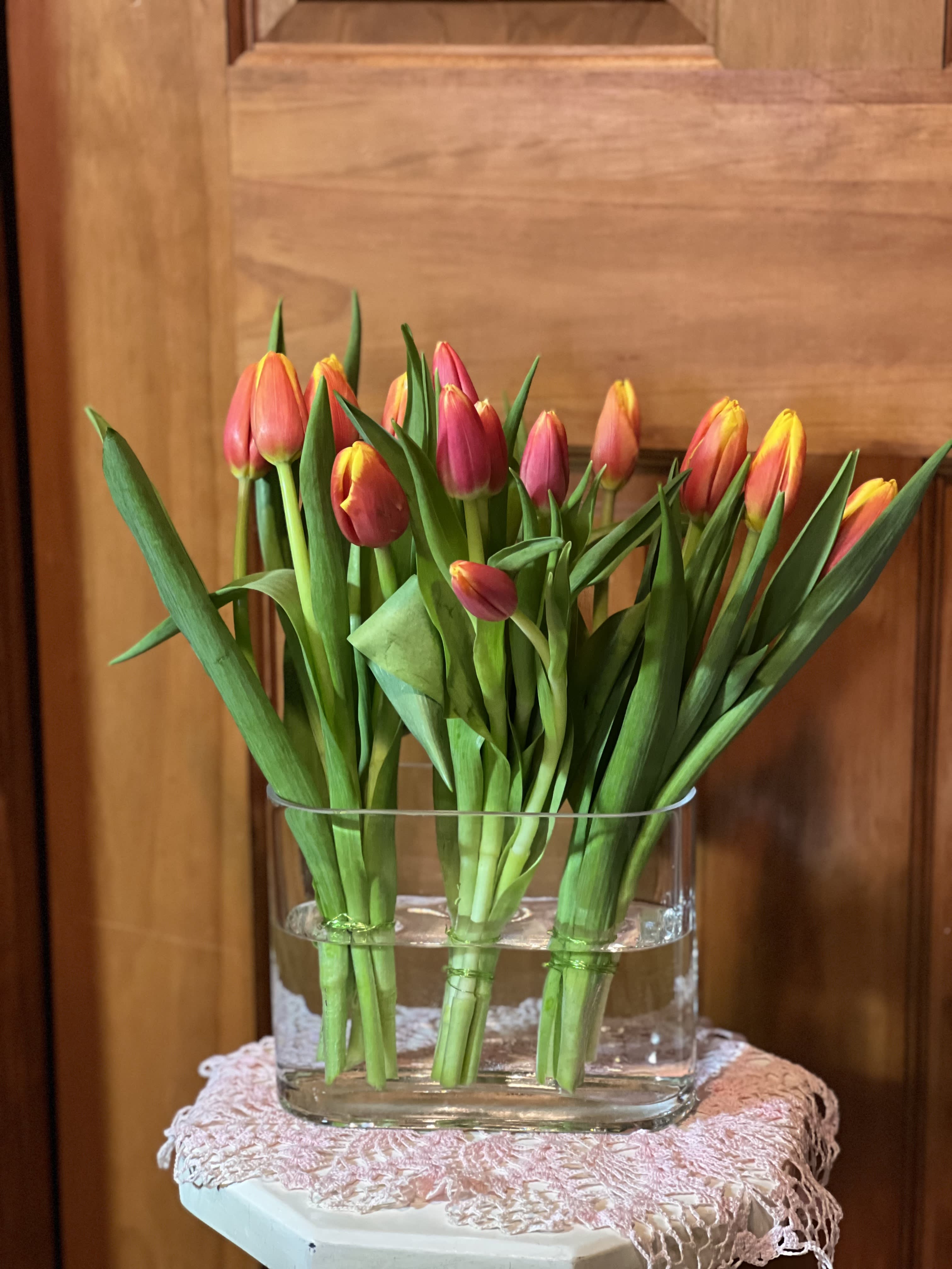 Grouping of Tulips - A grouping of Tulips in a clear oval 5 1/2" tall and 6 1/2" wide glass vase. 3 groups of tulips banded with wire. Tulips colors based on availably. ( 3 sets of 5 tulips each) 15 tulips total. 