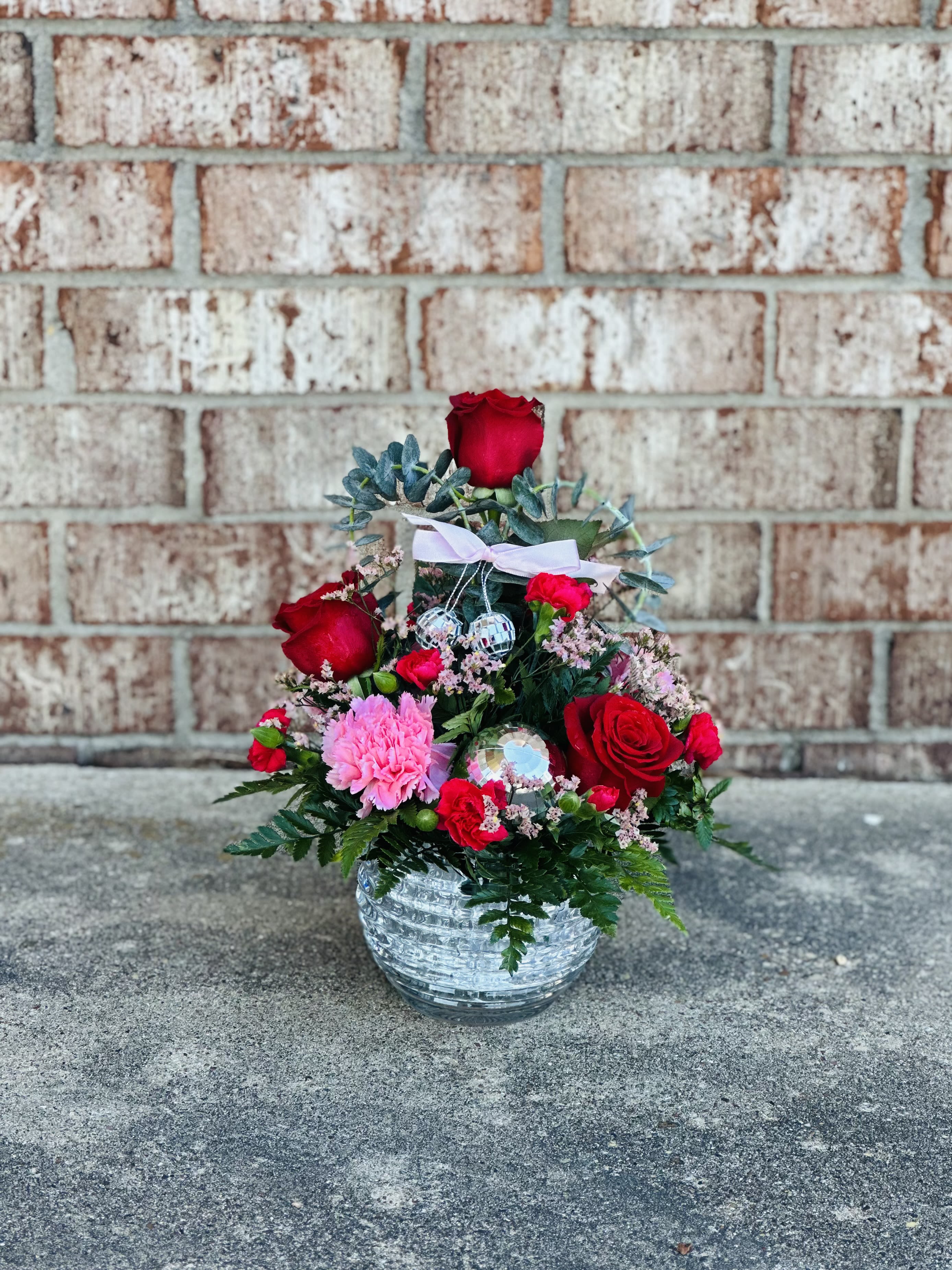 Disco Baby - Disco Baby is a little glam, a little sweet, and a whole lot of fun.  Designed in a textured crystal bowl, this arrangement pairs classic red roses with soft pink carnations, pops of baby blue accents, and playful mini disco balls for just the right amount of sparkle. Finished with lush greenery, it’s the perfect mix of romance and whimsy made for someone who loves tradition with a twist.   Ideal for Valentine’s Day, celebrations, or anyone who believes love should shine. 
