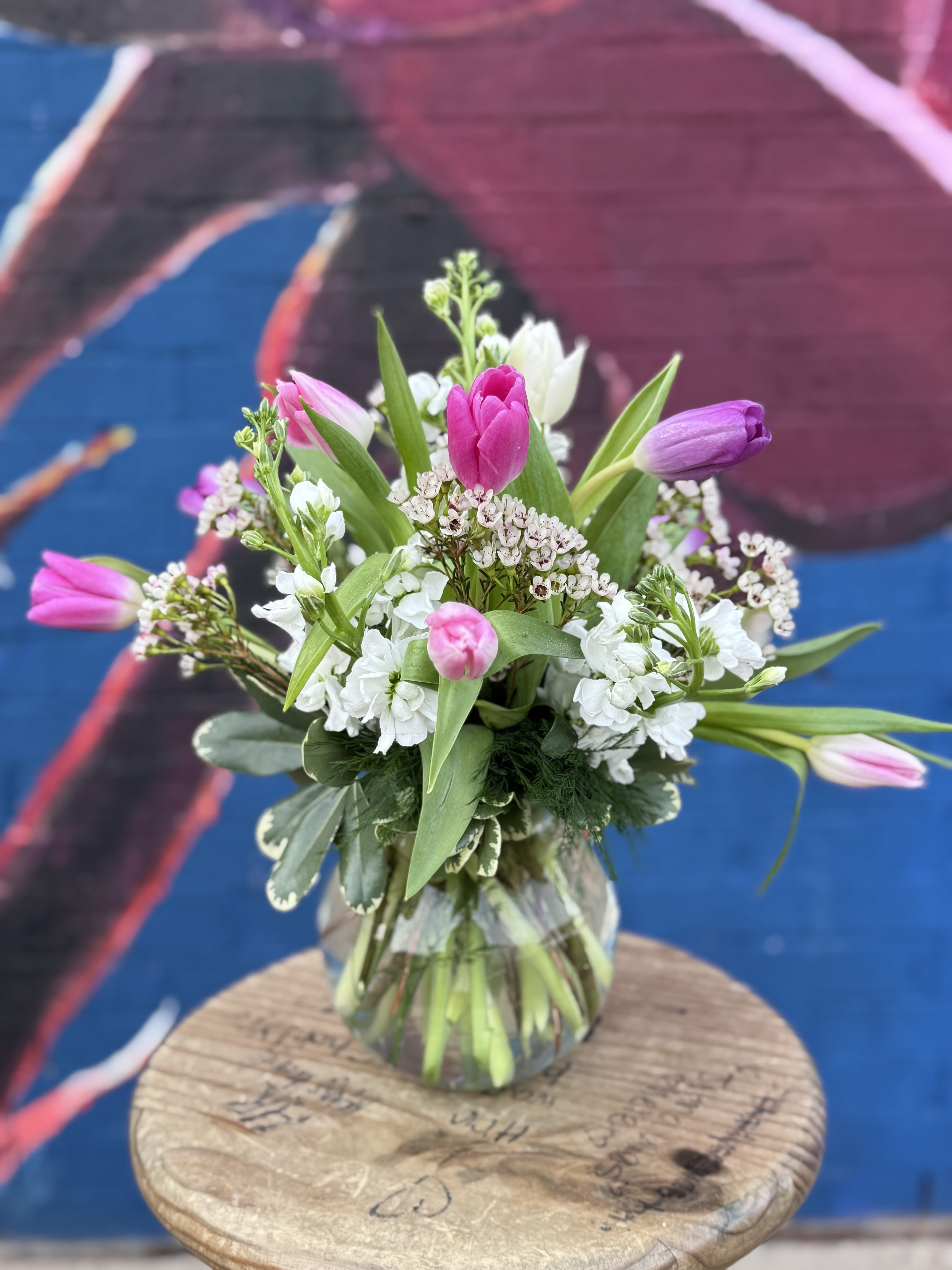 Tulip Mania - Fresh, joyful, and effortlessly elegant—Tulip Mania is a celebration of love in full bloom. This arrangement features a lively mix of pink and white tulips, accented with fragrant stock and soft greenery, all gathered in a classic Murano glass vase. Light, airy, and full of movement, it’s perfect for the Valentine who loves something fresh, modern, and a little unexpected.  A beautiful choice for new love, longtime love, or simply reminding someone how much they brighten your world.