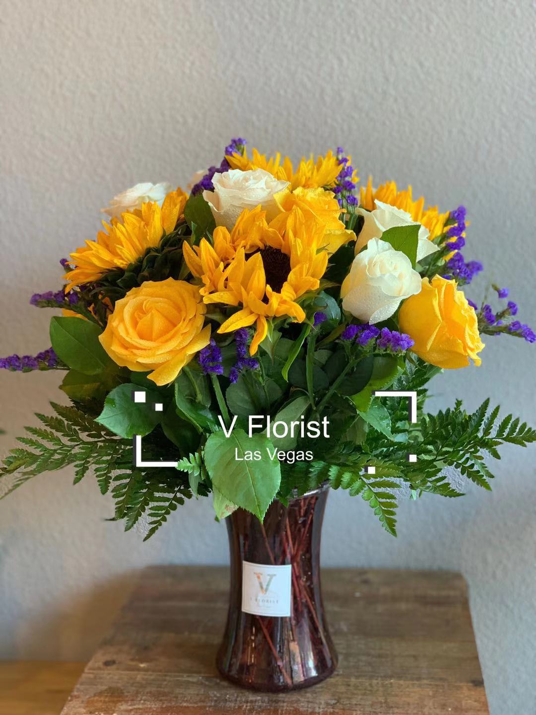 Cheerful Sunflower Arrangement  - A bright and cheerful bouquet made with sunflowers, yellow roses, white roses, and purple statice. Perfect for brighten ups someone's day.  Our florists select the freshest flowers available, so colors and varieties may vary due to local availability.