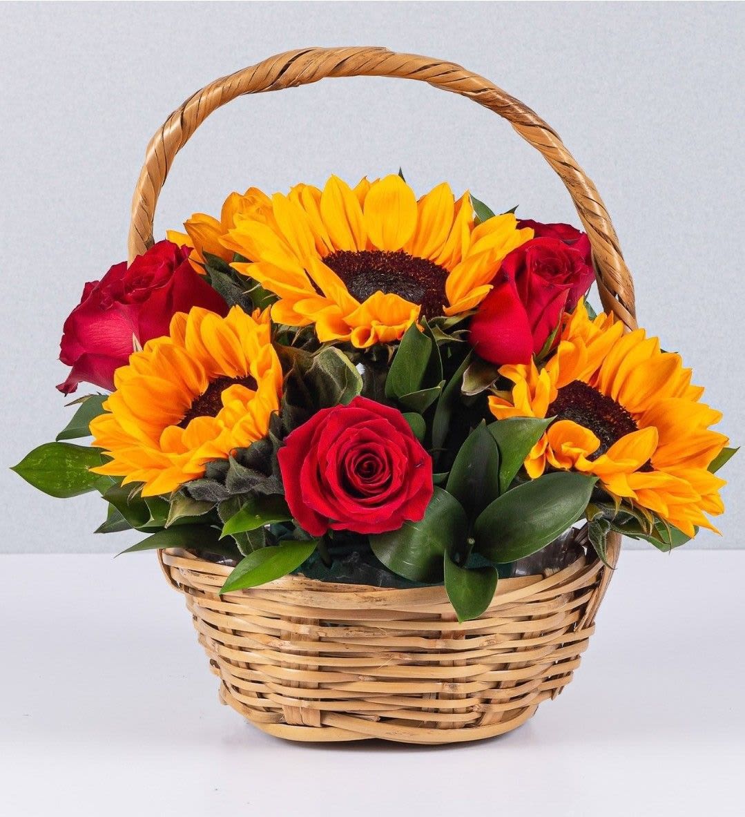 Sunflower &amp; Red Rose Love Basket - A radiant and romantic floral basket featuring vibrant sunflowers and classic red roses, beautifully arranged with fresh greenery in a natural wicker basket. This design combines warmth, love, and elegance — perfect for Valentine’s Day, anniversaries, or surprising someone special with a bright and joyful gesture.