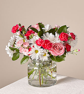 Sweet Surprises® Bouquet - The Sweet Surprises® Bouquet was created to spread love and caring kindness wherever it might be sent! Hot pink and pale pink mini carnations pop with their blushing hues, arranged amongst the clean white petals of traditional daisies and lush greens. Presented in a clear glass vase, this gorgeous fresh flower arrangement brings a fresh excitement to your special recipient's day, whether it is sent for a special occasion, such as a birthday, or simply to let them know how much you care. Bouquet is about 14"H by 15"W. For long–lasting blooms replace water and trim stems daily. The bouquet pictured reflects our original design for this product. While we always try to follow the color palette, we may replace stems to deliver the freshest bouquet possible, and we may sometimes need to use a different vase.