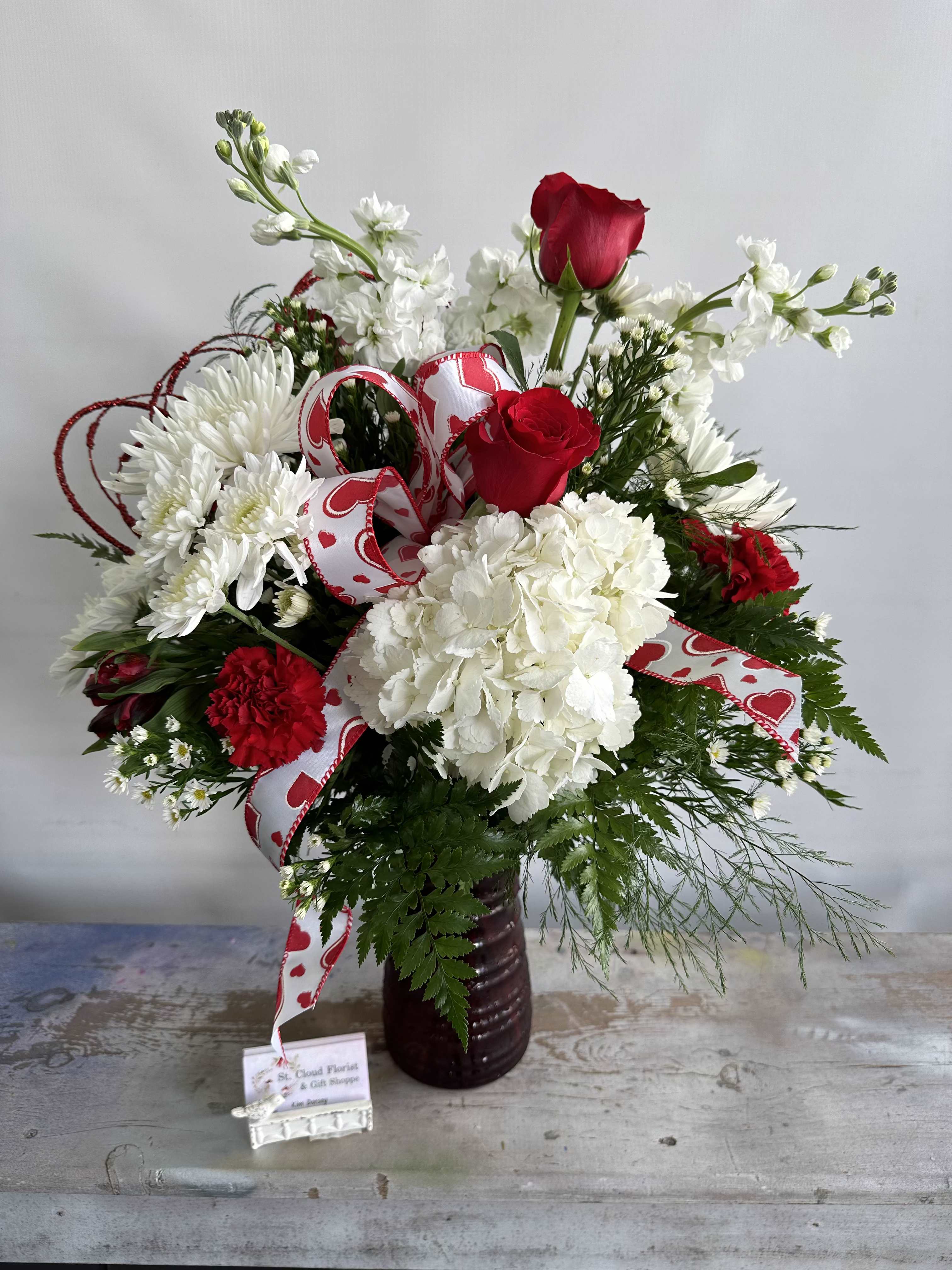Love Potion - An elegantly classic arrangement of hydrangeas, red roses, and accent flowers. Arrangement comes in 10" Red Vase. While supplies last. Flowers and containers are subject to substitution.