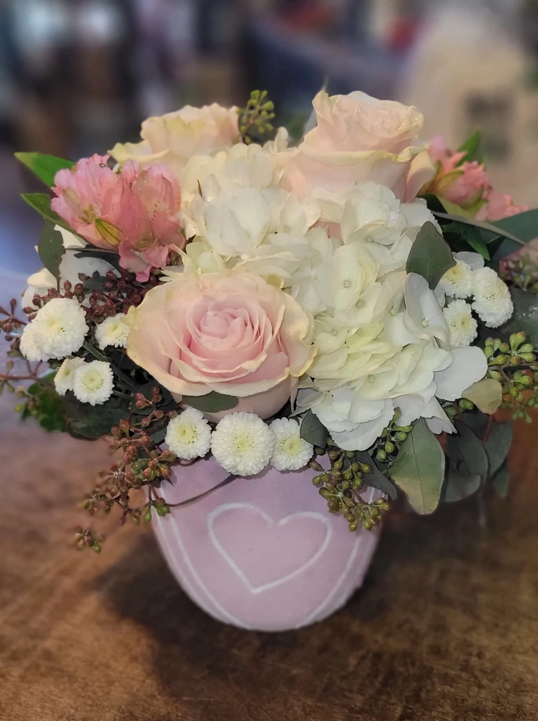 Love's So Sweet - Such a sweet bouquet of white hydrangea, pink roses, pink alstroemeria, and white buttons with assorted greenery arranged in a light pink heart decorated concrete pot. **Container varies while still having pink and white with hearts***