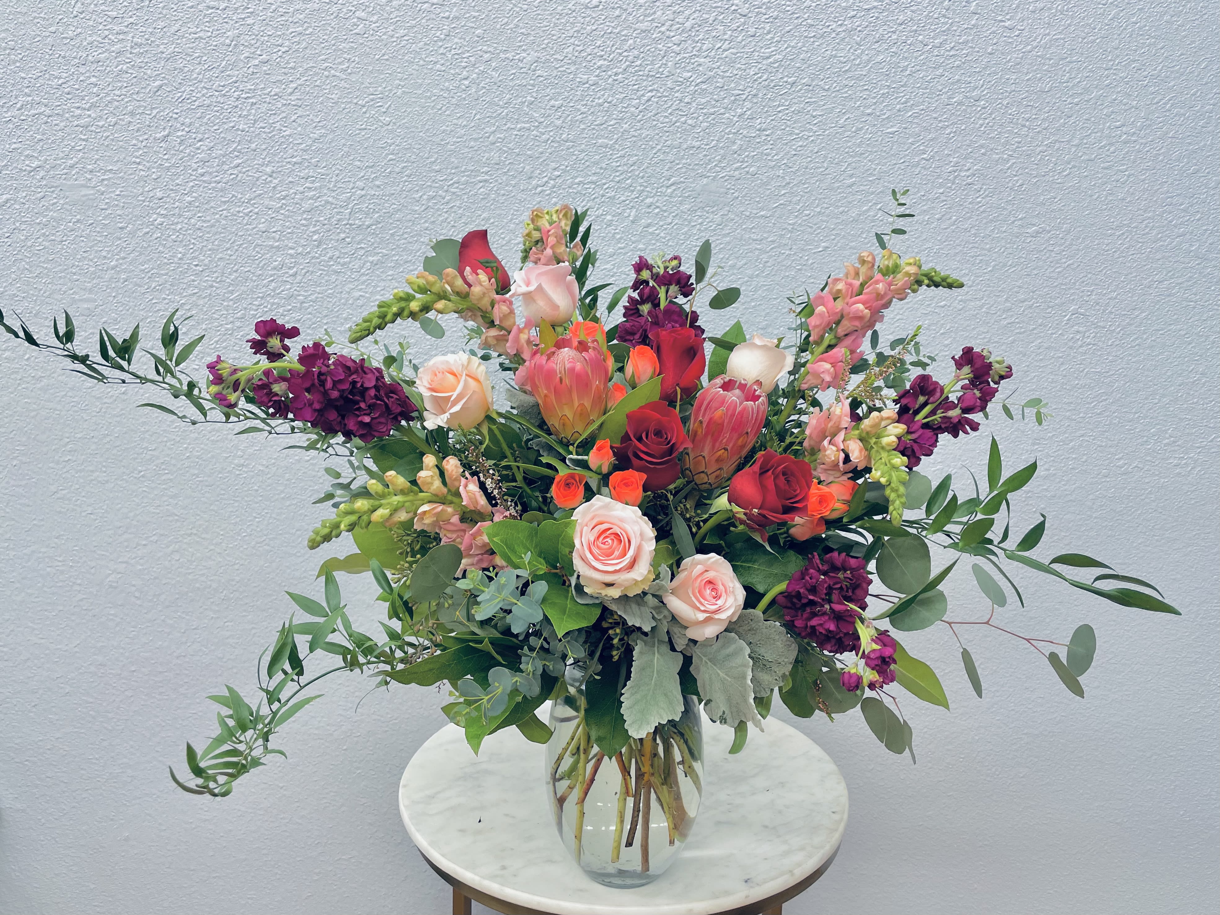 Francine - Color Palette: burgundy, red, pink, blush, cream This bouquet is the classic romantic gift! Perfect for Valentine's Day or any romantic occasion!  Queen protea, snapdragons, stock and roses in girly hues tucked into botanical eucalyptus and seasonal greens. *Photo shows deluxe upgrade*