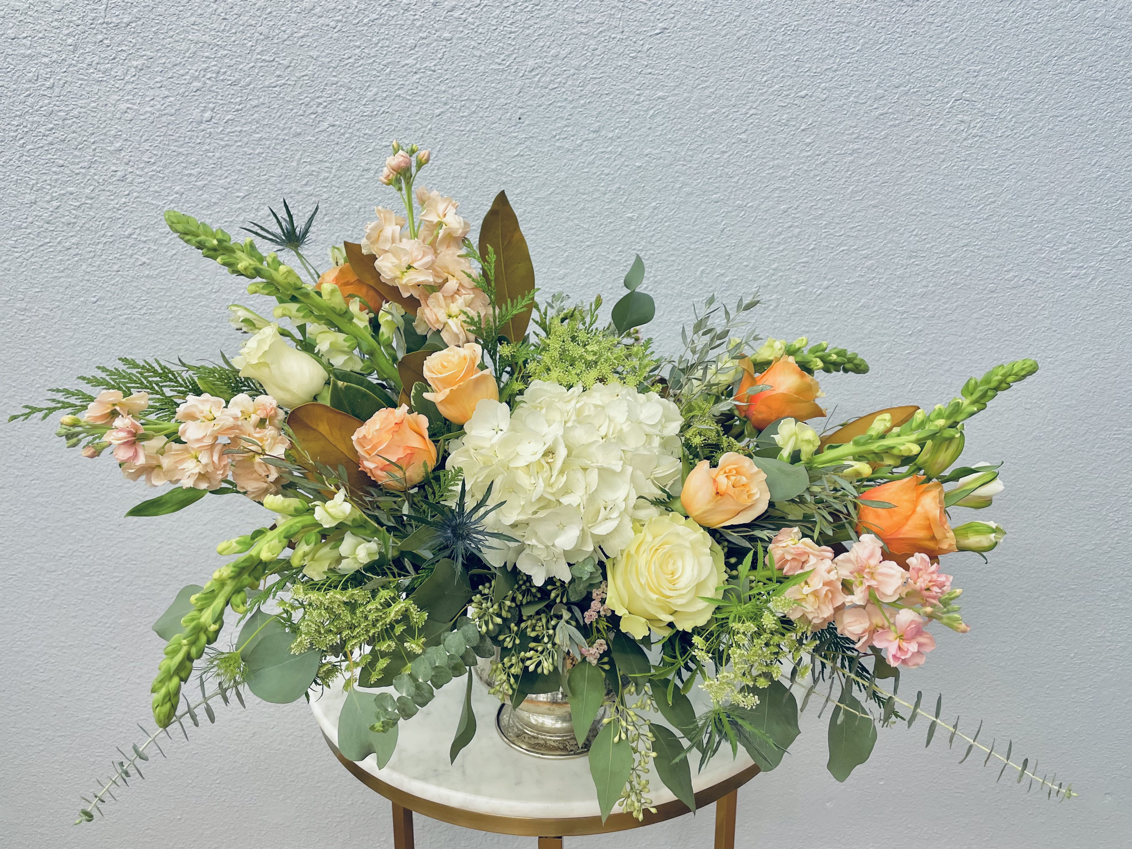 Lydia - Color Palette: white, cream, blush, peach Soft feminine tones of white, peach, blush and apricot stock, rose, hydrangea and Veronica nestled into botanical eucalyptus, magnolia and seasonal greens in simple silver vase.  *Photo shows deluxe upgrade*