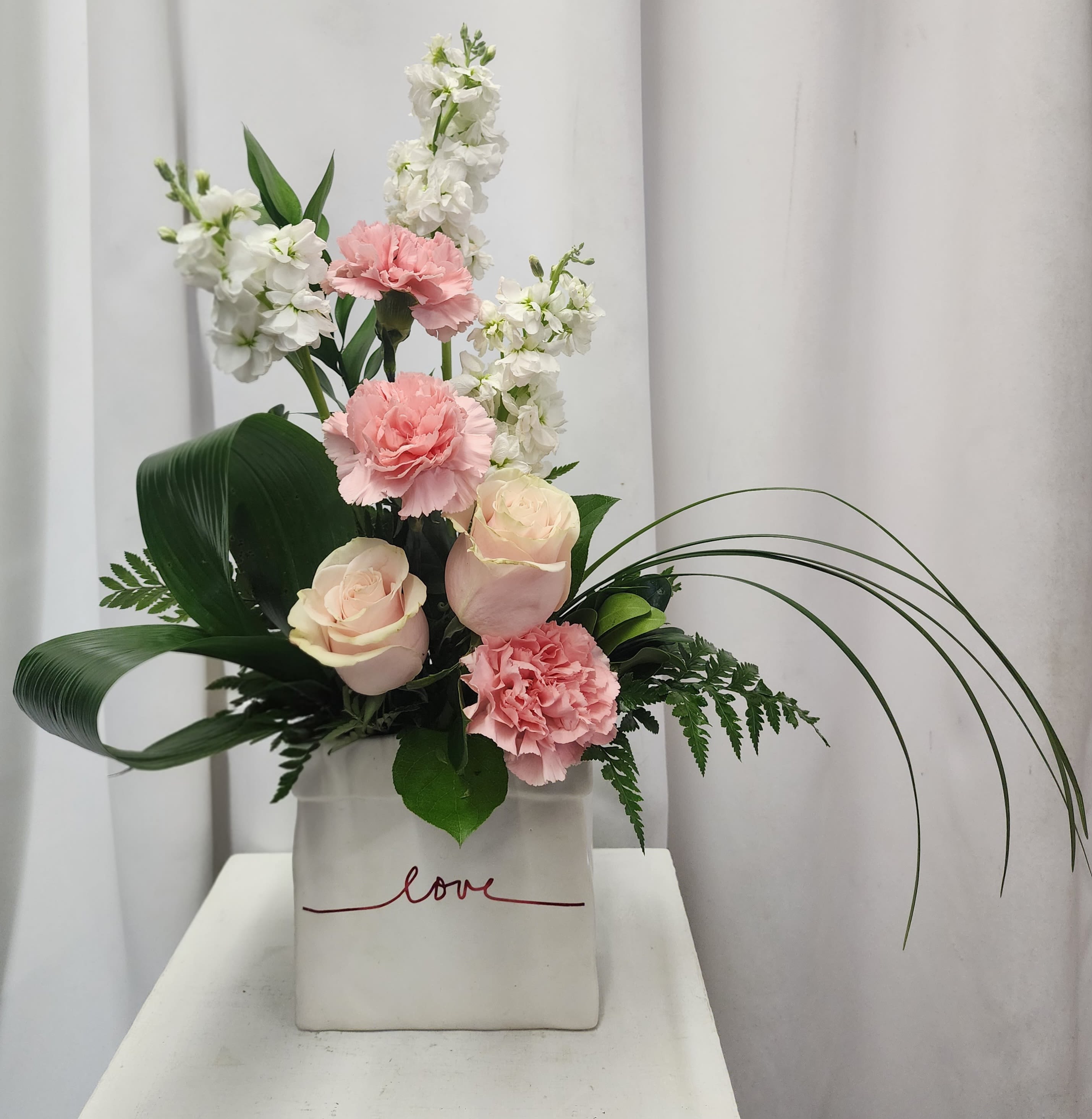 Love in Pink - Celebrate Love with this elegant floral arrangement with soft pink roses, pink carnations and white stock. Fragrant and surrounded by designer greens in a keepsake ceramic vase -  with “love” imprinted.  