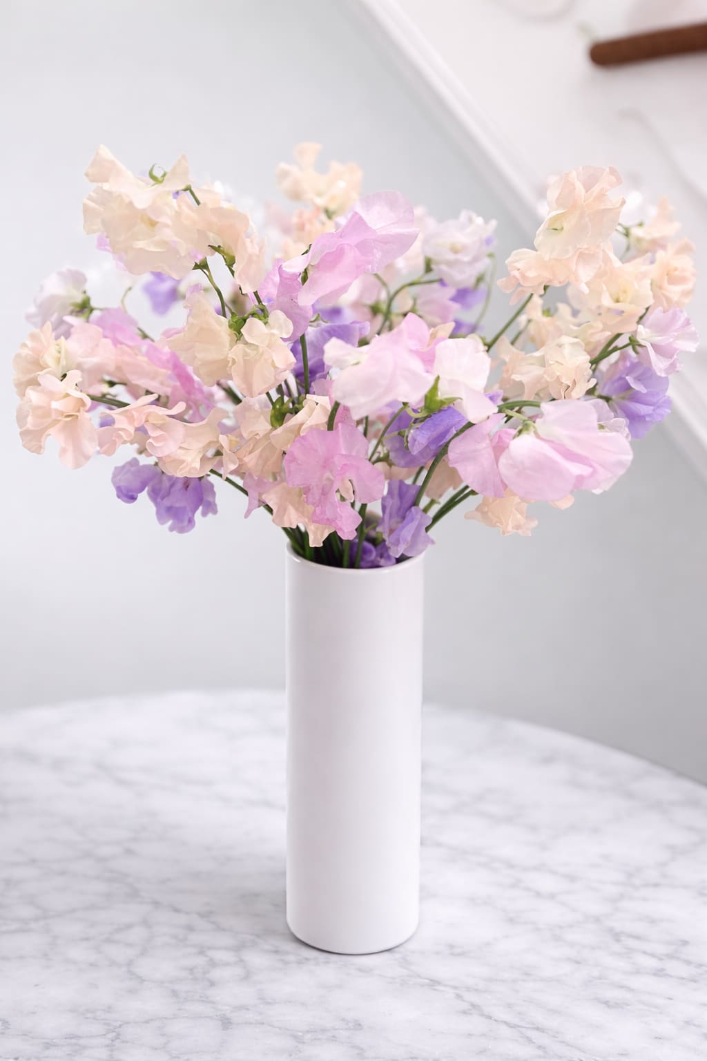 Morganite Afterlight - Soft, luminous, and quietly enchanting, Morganite · Afterlight captures the beauty of what lingers. Composed of delicate sweet peas in shades of light pink, blush, and pale lavender, this arrangement glows with an almost translucent quality — sheer petals catching the light as if illuminated from within.  Inspired by the gemstone morganite, long associated with tenderness, emotional clarity, and gentle strength, this design is romantic and refined. The sweet peas’ natural movement and ethereal texture create a sense of ease and intimacy, styled to allow their fleeting beauty to speak for itself.  Morganite · Afterlight is less about spectacle and more about feeling — a moment of softness, warmth, and grace that stays with you, even after the light begins to fade. Sweet peas are celebrated for their graceful movement, whisper-thin texture, and gentle color transitions. Styled simply in a clean white vessel, this arrangement allows their natural beauty to shine — feeling both refined and ethereal, with an understated sense of luxury.  Perfect for moments that call for understated beauty, quiet romance, or a thoughtful, elevated gesture. Ideal for Valentine's Day, Mother's Day, and everyday.  Please note: Sweet peas are seasonal and inherently delicate. Variations in color, shape, and movement are part of their natural charm. Arrangement can be ordered with choice of color(s); please indicate choice in the comments section. Upgraded arrangements will include additional stems.