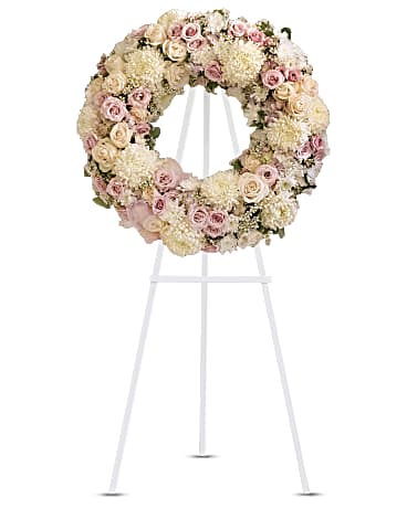 Peace Eternal - A pure and delicate expression of adoration. Accented with a sheer pink organza bow, this wreath of white, crème, and pale pink petals gently embraces loving memories, and offers solace and sweet thoughts at a time of loss. Lovely blooms such as crème and pink roses, pink hydrangea and white chrysanthemums are nestled together and accented with organza ribbon. A touching