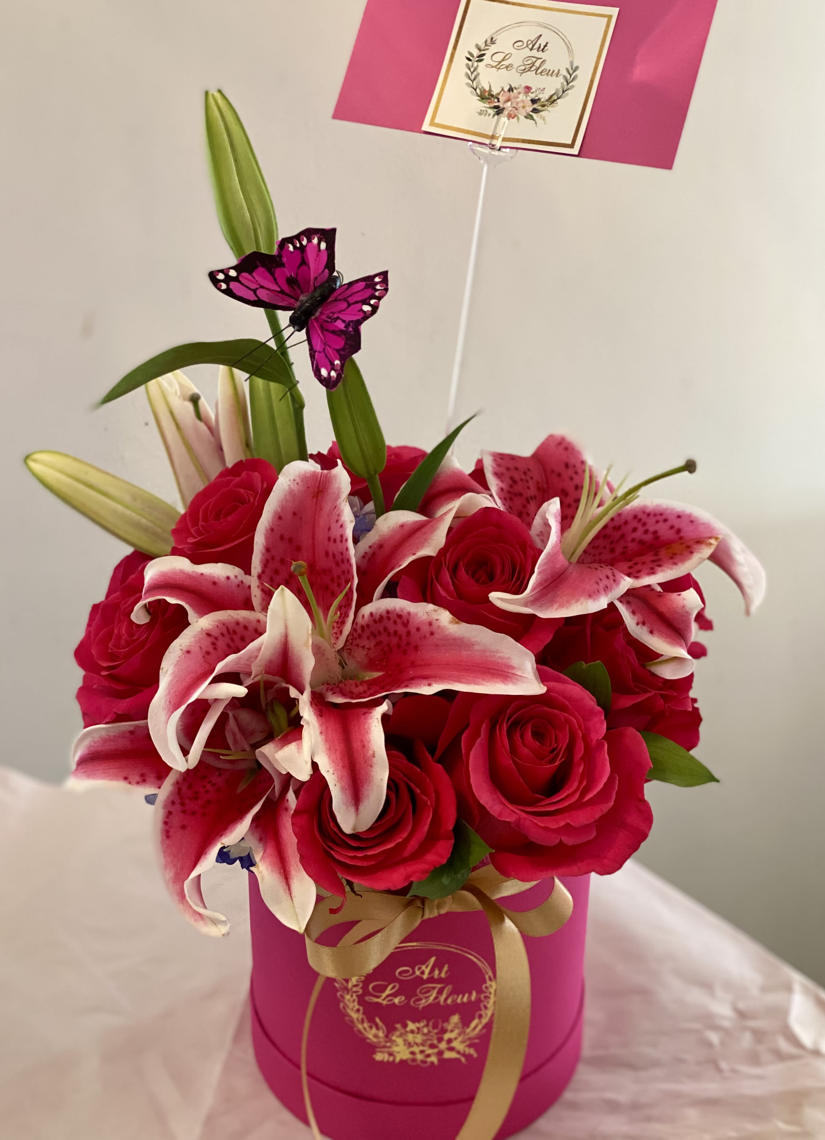 Pretty in Pink- Valentines Exclusive - A chic mini hatbox overflowing with bold hot pink roses, accented by fragrant stargazer lilies and fresh greenery—vibrant, elegant, and made to wow. 