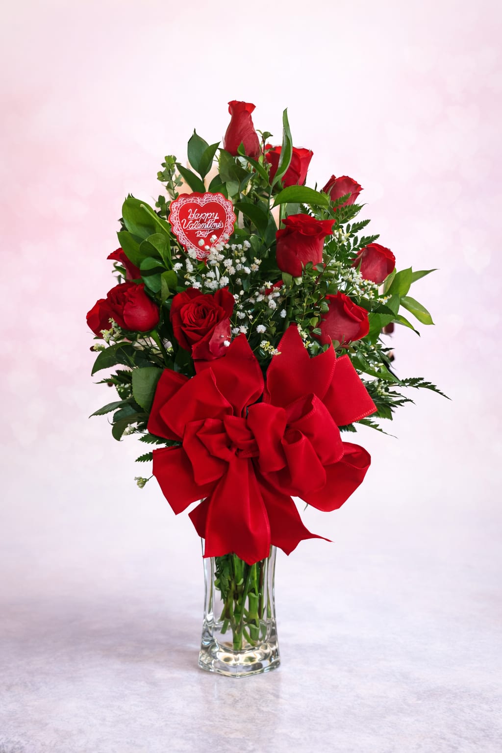 Classic Valentine Elegance  - Classic Valentine Elegance is a timeless expression of love, featuring rich red roses accented with delicate white baby's breath and lush greenery. Designed in a clear glass vase and finished with a bold satin bow and Valentine keepsake, this arrangement is perfect for conveying heartfelt romance and lasting affection. 