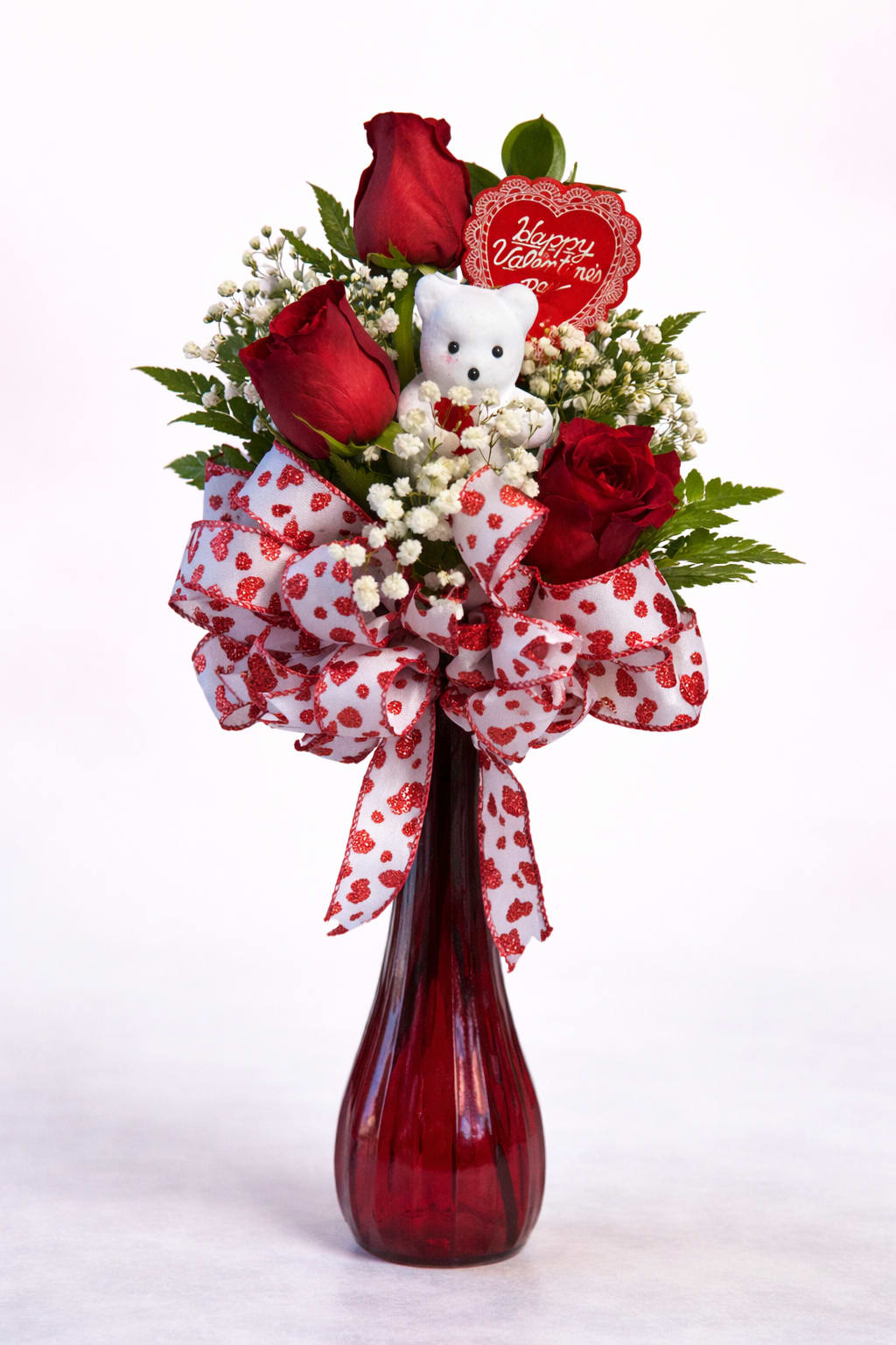 Sweetheart Surprise - Sweetheart Surprise is a charming Valentines Day arrangement featuring classic red roses nestled among delicate baby's breath and luscious greenery. Finished with a festive heart ribbon, a keepsake teddy bear, and Valentine accent, this design is perfect for spreading love, smiles, and warm hugs.