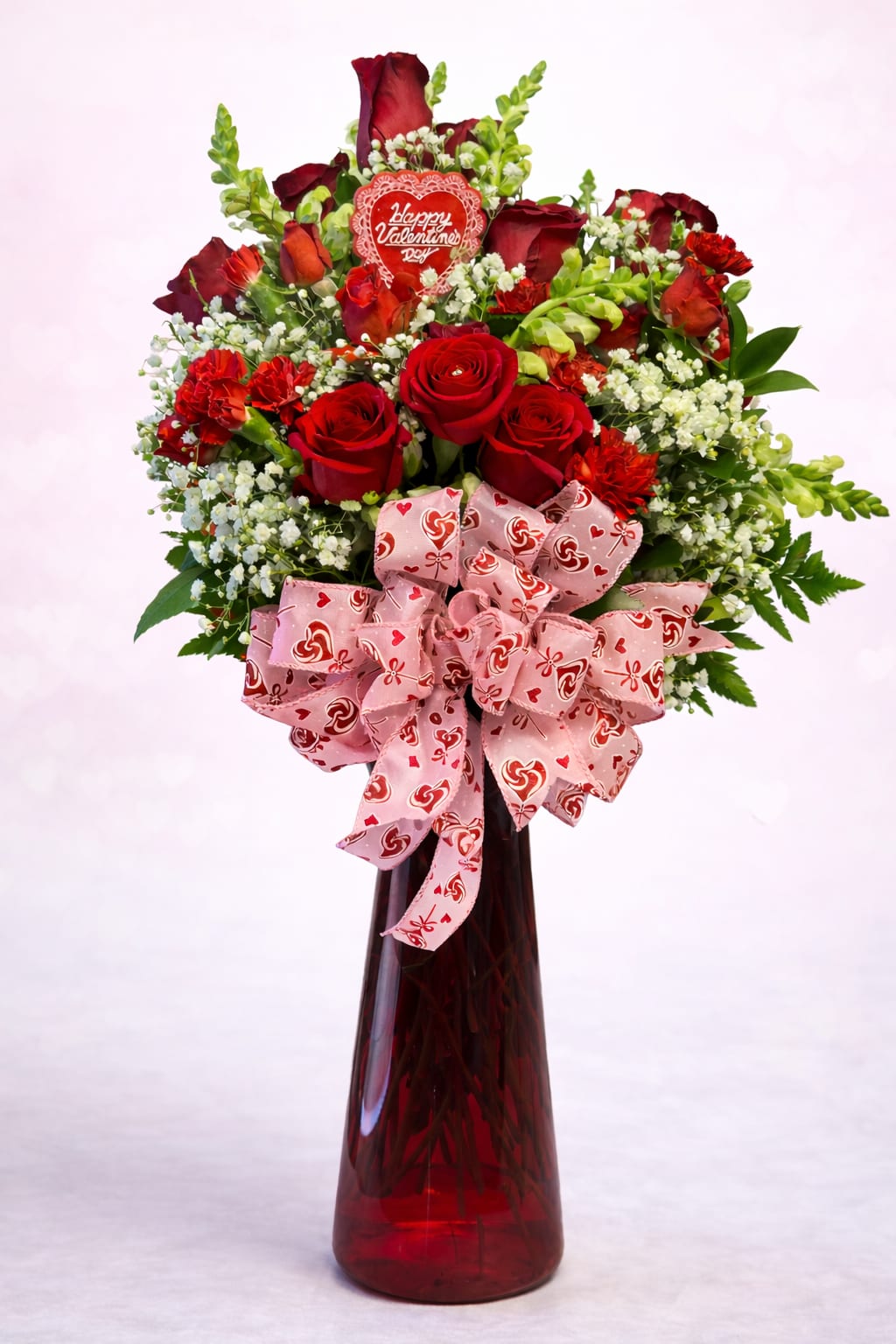 Crimson Romance - Crimson Romance is a lush Valentine's day arrangement overflowing with rich red roses, vibrant red Carnations and beautiful snap dragons and delicate baby's breath, all accented with fresh greenery and finished with a festive Valentines bow. Designed in an elegant glass vase this arrangement makes a bold and heartfelt statement of love, passion and devotion.