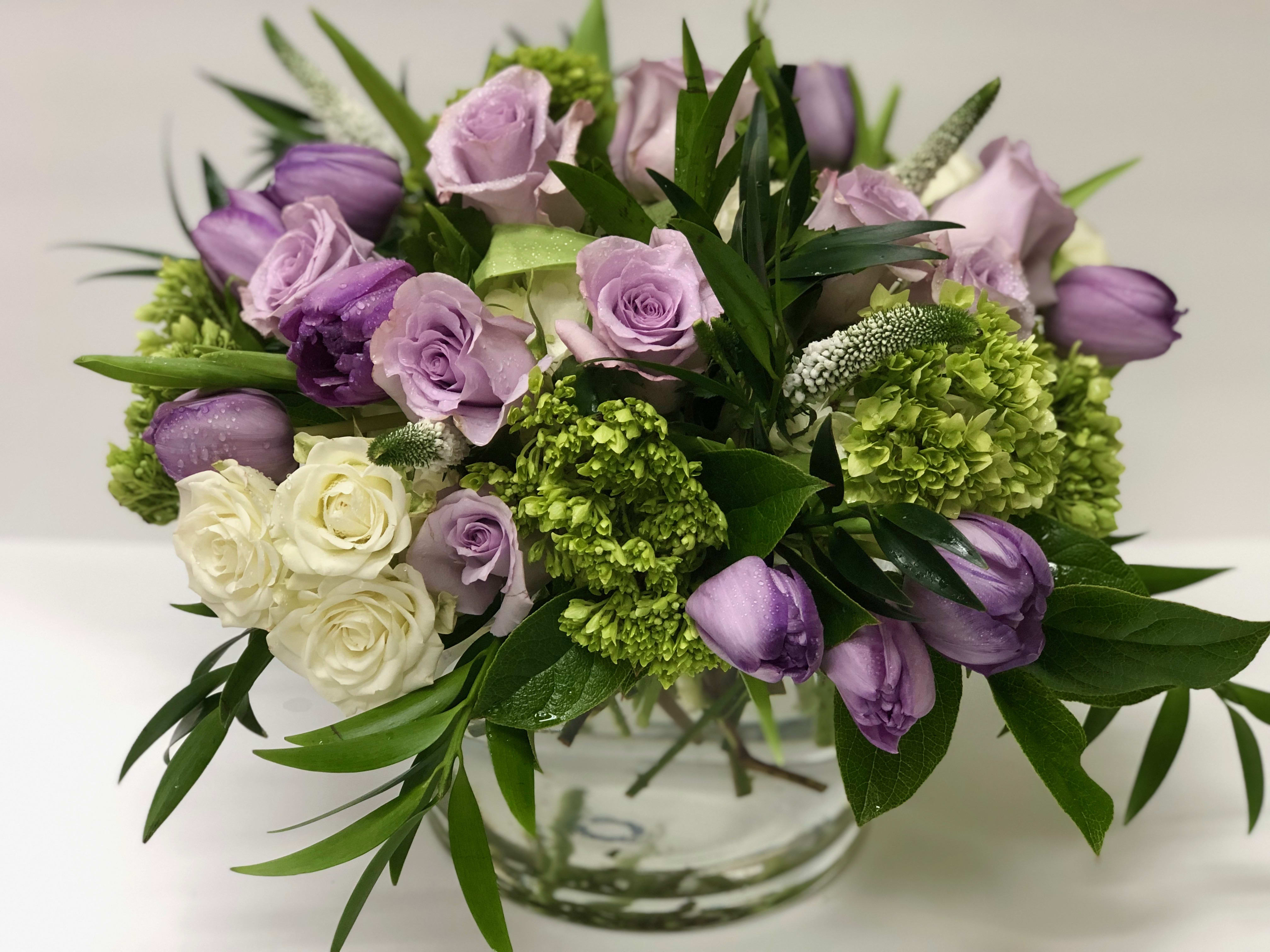 VIOLA - Vibrant hues and enchanting textures meet in this exquisite floral design. Here, ruffled lavender tulips dance around exotic stems of light purple roses and other charming greens. Perfect for any occasion. 