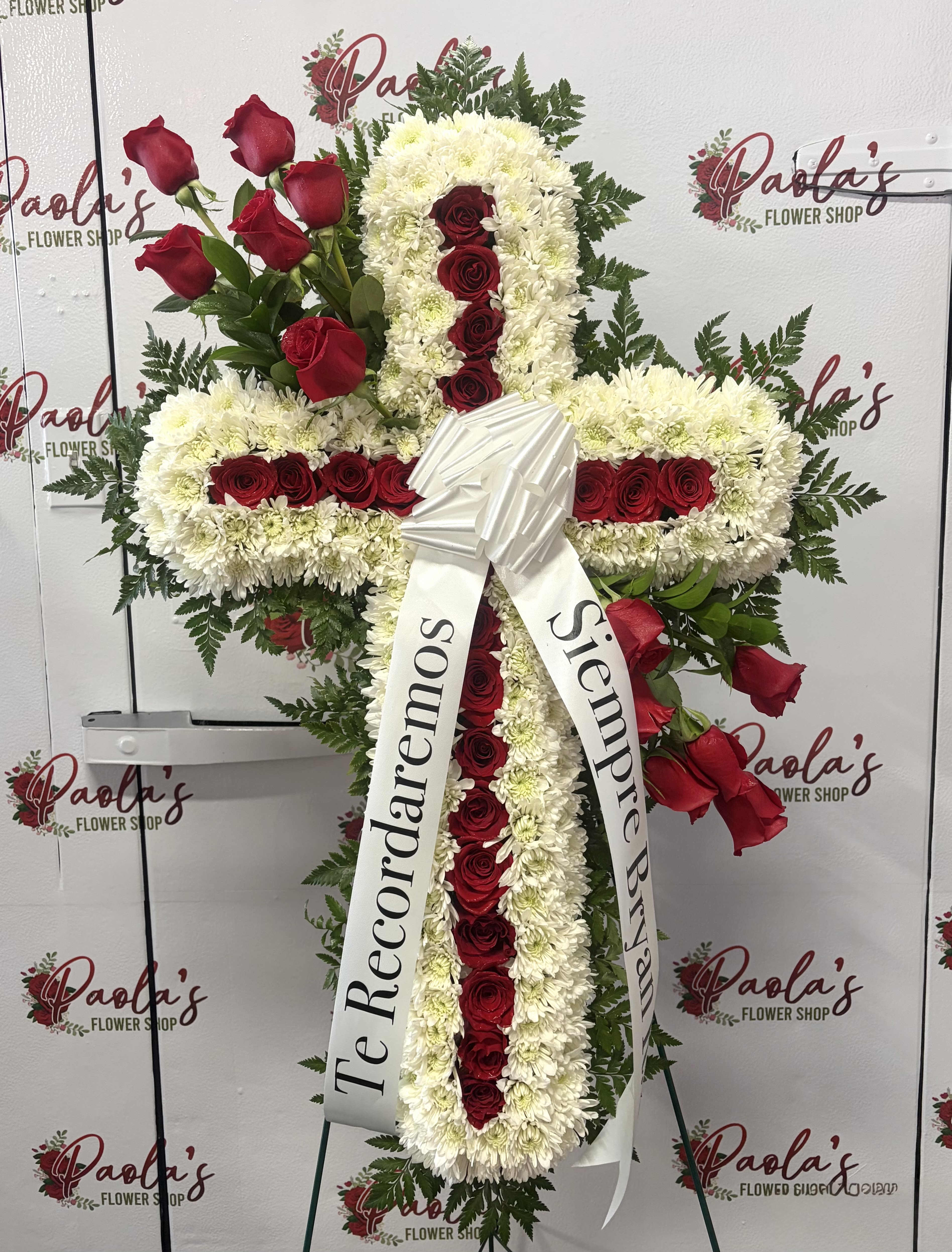 Forever in Faith Sympathy Cross - Honor a life remembered with grace, love, and devotion. Our Forever in Faith Sympathy Cross is a handcrafted standing cross arrangement designed to express deep condolences and eternal remembrance. Created with fresh white chrysanthemums symbolizing purity and peace, and accented with rich red roses representing love and respect, this elegant tribute offers comfort during times of loss.  Displayed on an easel and finished with a customizable ribbon, this floral cross is ideal for funeral services, memorials, or celebrations of life. 
