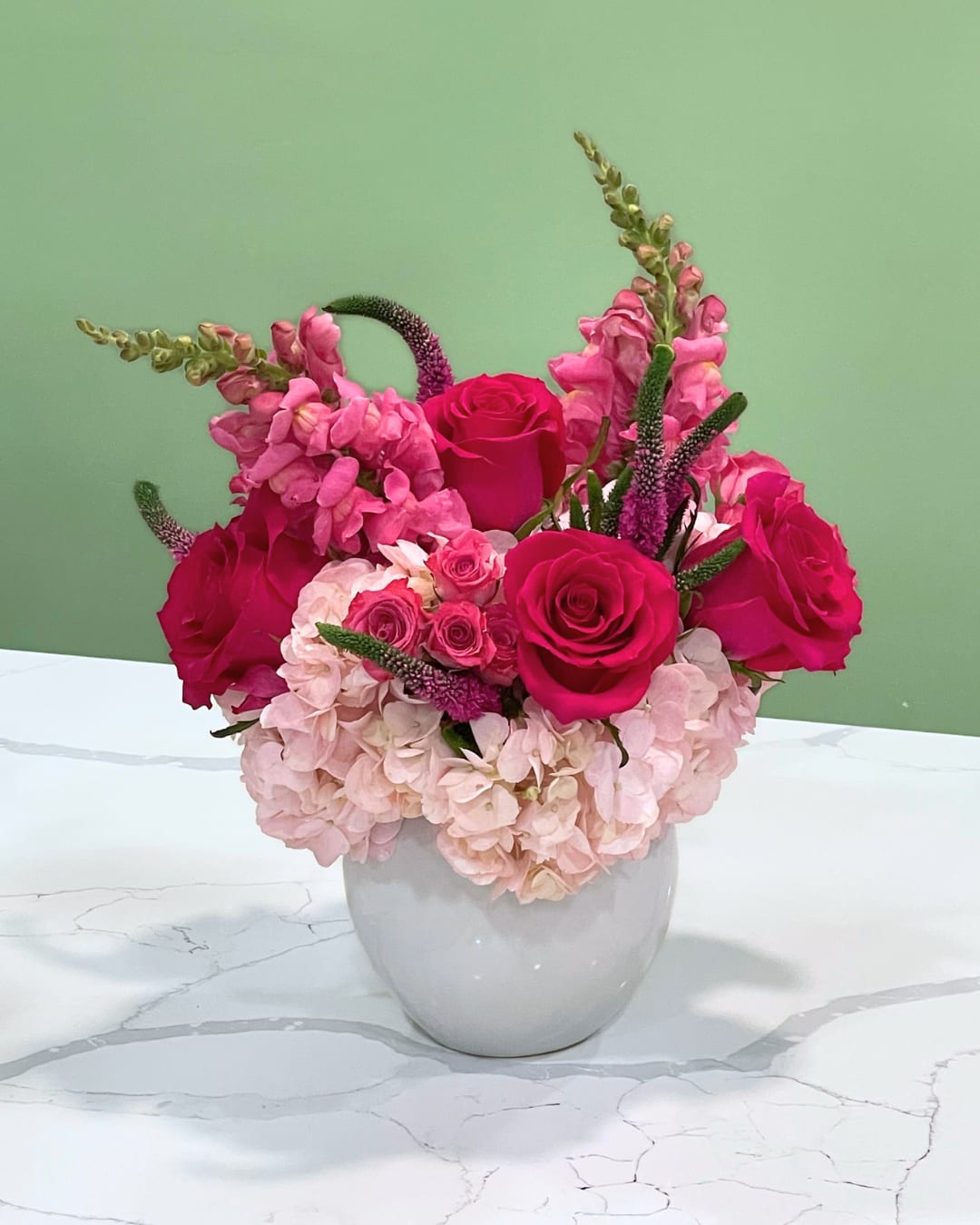 Rose Quartz - This lively barbie pink arrangement has light pink hydrangeas, hot pink roses, spray roses, veronicas and snapdragons in a white ceramic vase. 