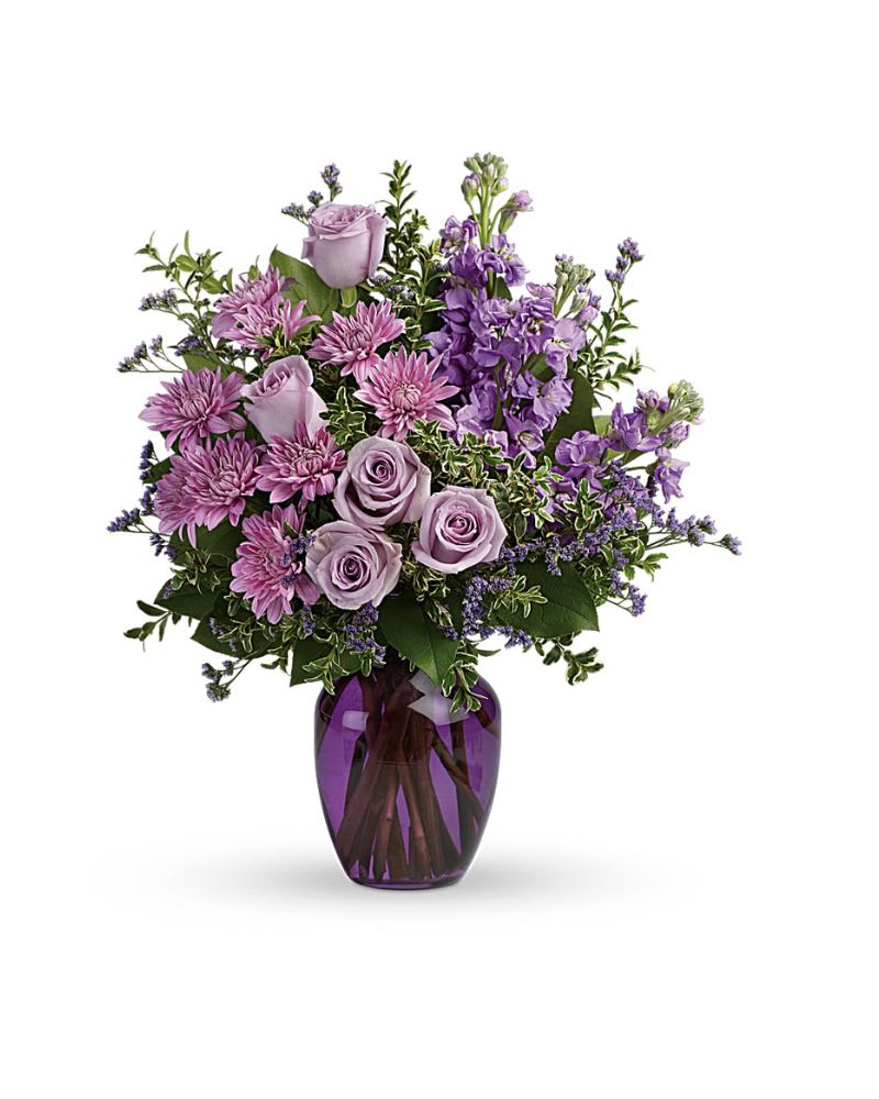 Together At Twilight Bouquet - The perfect pick for the purple lover in your life! This impressive bouquet charms with roses, stock and mums. Presented in a gorgeous glass vase. This dramatic arrangement includes lavender roses, lavender stock, lavender cushion spray chrysanthemums, lavender limonium, oregonia and lemon leaf. Delivered in a purple glass vase
