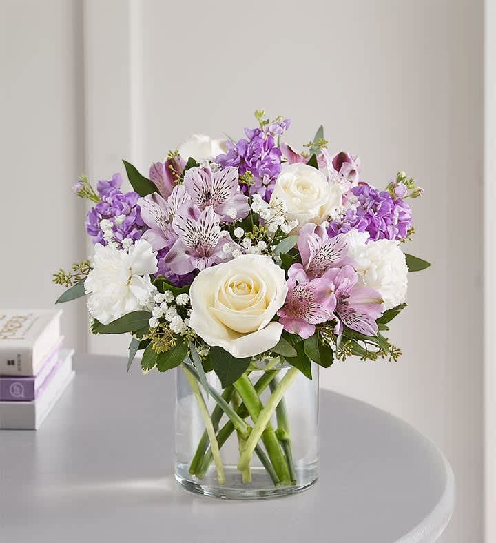 Lovely Lavender Medley™ - Lovely memories are made with thoughtful gifts for the ones we care about. Our charming bouquet is loosely gathered with a medley of lavender &amp; white blooms. Hand-designed inside a clear cylinder vase with cascading greenery all around, it’s a wonderful way to express the sentiments you have inside your heart. All-around arrangement with white roses and carnations; lavender Peruvian lilies (alstroemeria) and stock; accented with baby’s breath, seeded eucalyptus and assorted greenery