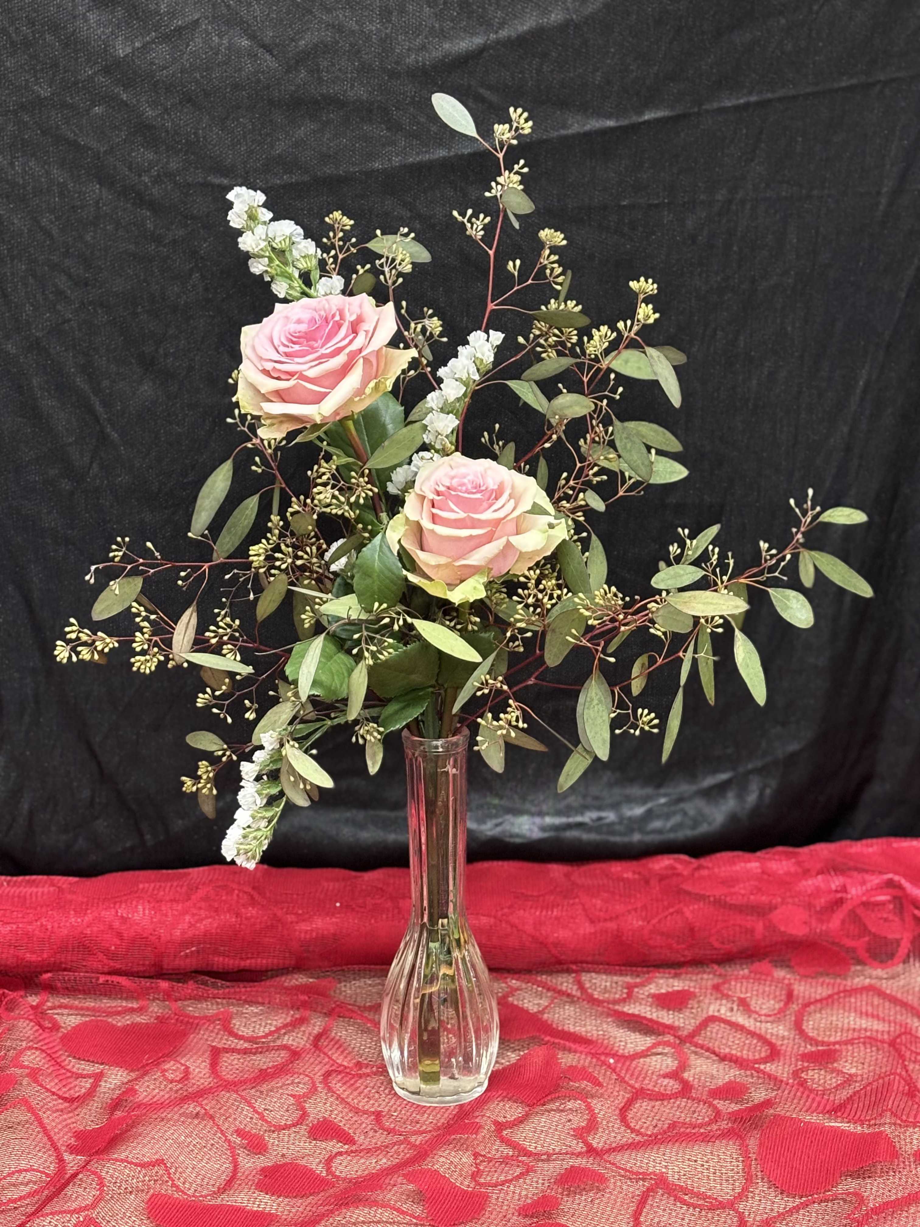 Sweet Simplicity - Delicate and charming, this petite arrangement features two light pink roses accented by soft, textured seeded eucalyptus. A perfect gesture of grace and thoughtfulness, it's ideal for small celebrations of heartfelt moments.