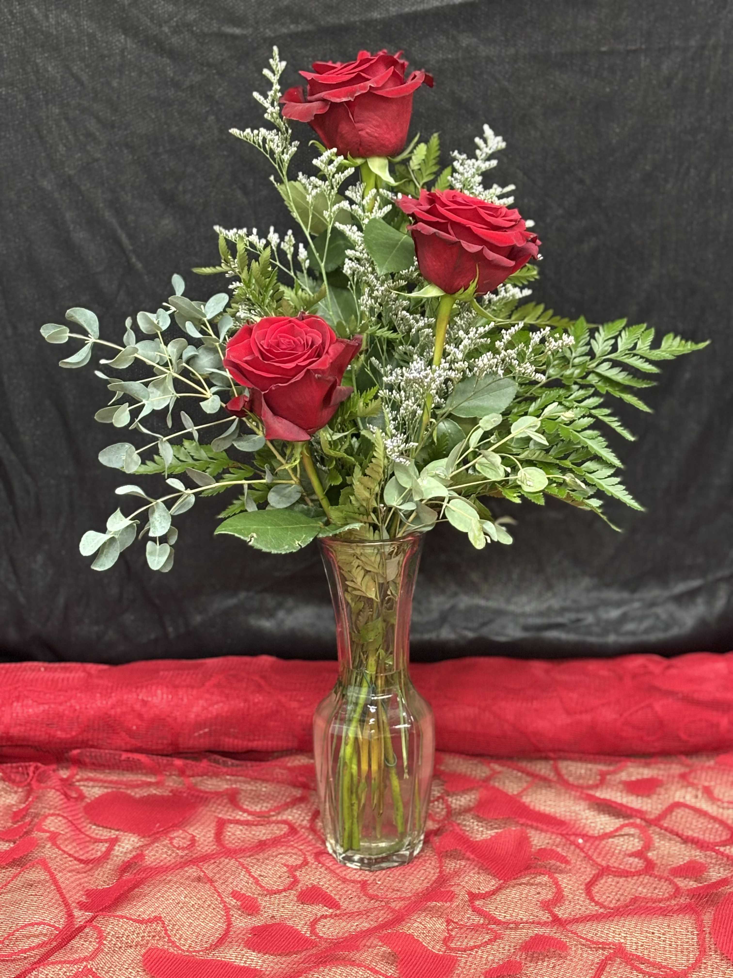 Triple Flame - Bold and romantic, this arrangement showcases three stunning red roses, symbolizing love, passion, and commitment. Accented with lush greenery, it's a timeless expression of heartfelt emotions, perfect for any occasion. Greens and filler may vary by availability. 