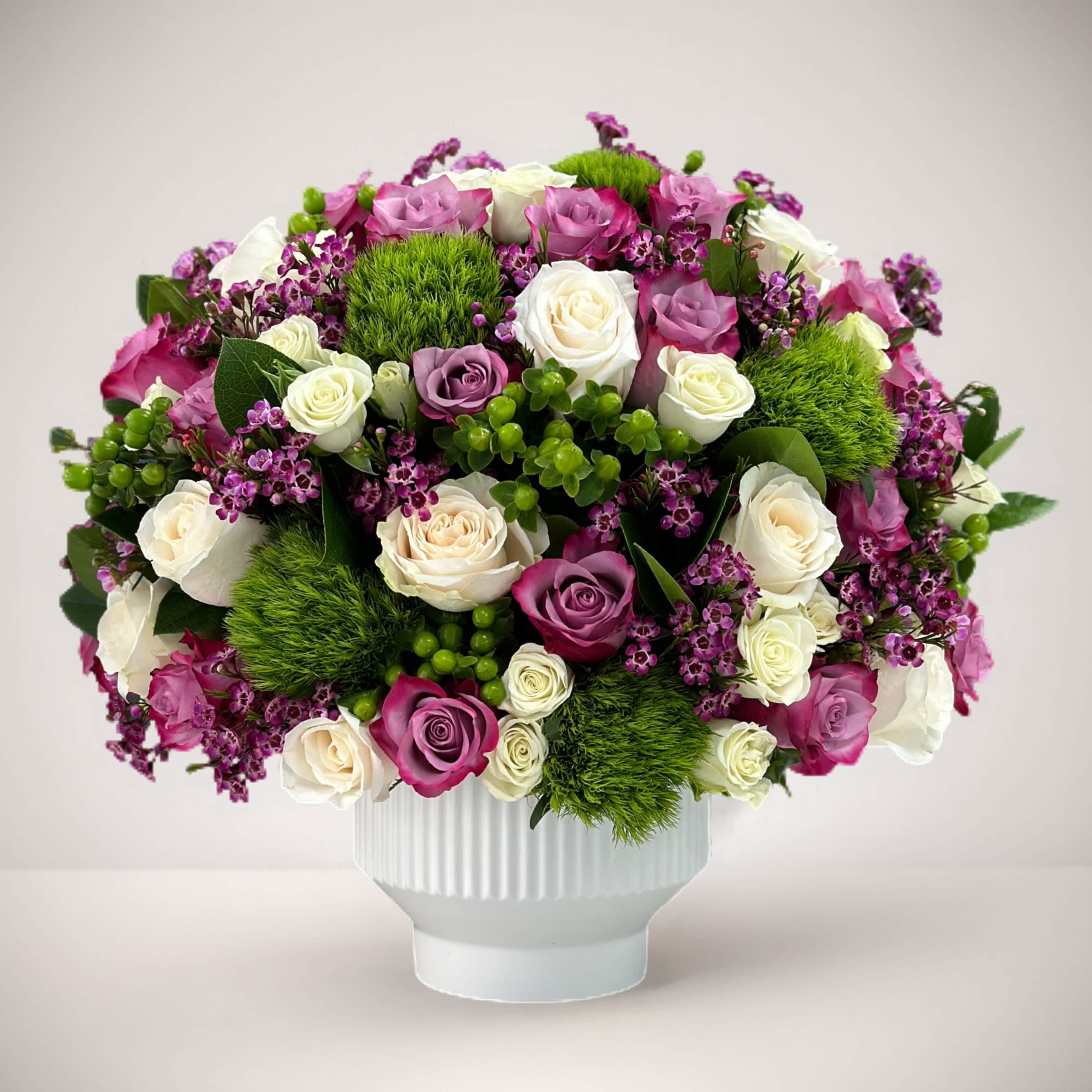 Enchanting Harmony - Evoke a sense of timeless elegance and natural beauty with our exquisite flower arrangement featuring a pristine white vase adorned with a captivating combination of purple and white roses, delicately accented with lush greenery. This arrangement seamlessly blends sophistication with nature's grace, creating a captivating centerpiece that will mesmerize all who behold it.