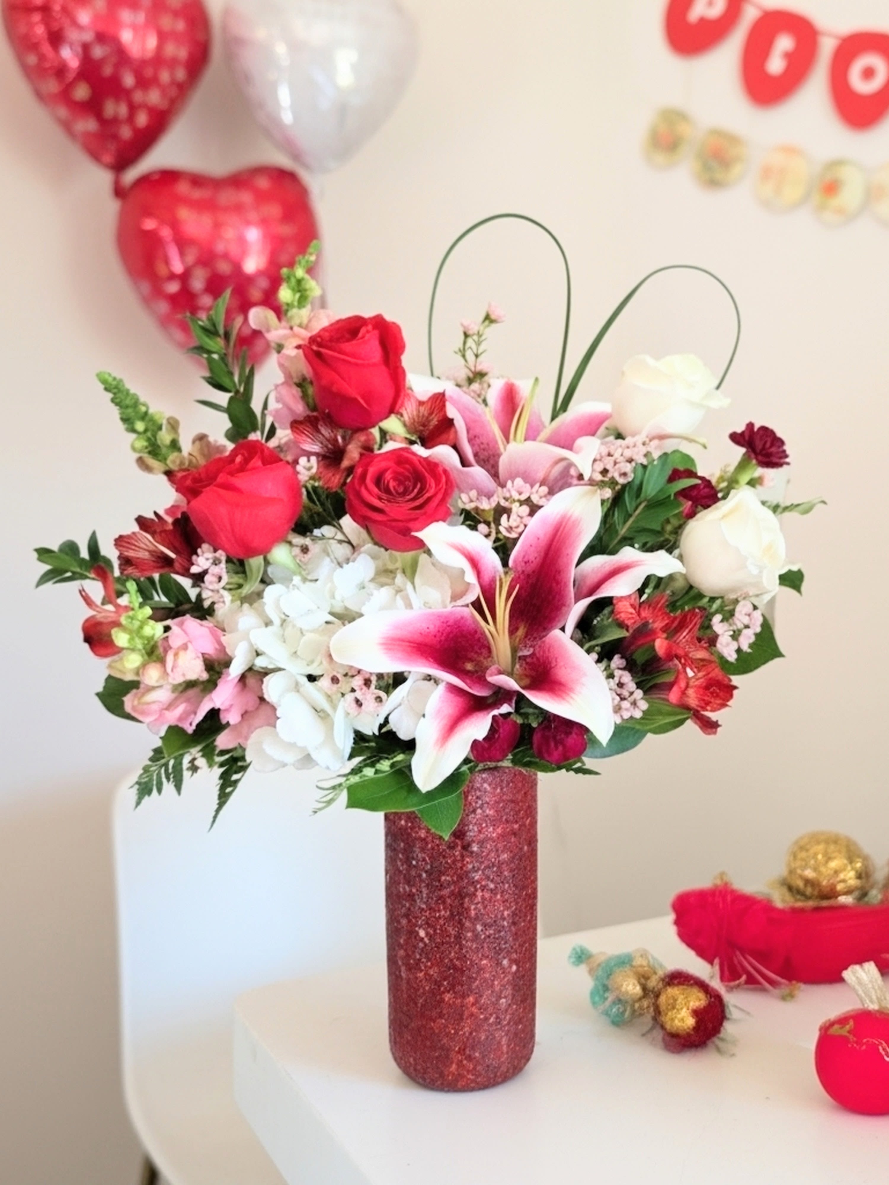 Be Mine Bouquet - Red Crackled glass vase designed in a semi asymmetrical style. This gorgeous  bouquet is a mix or red rose, white roses,  hydrangea, mini canrs, alstoemeria,  pink snap dragon, pink lilies and of course a lily grass heart. 