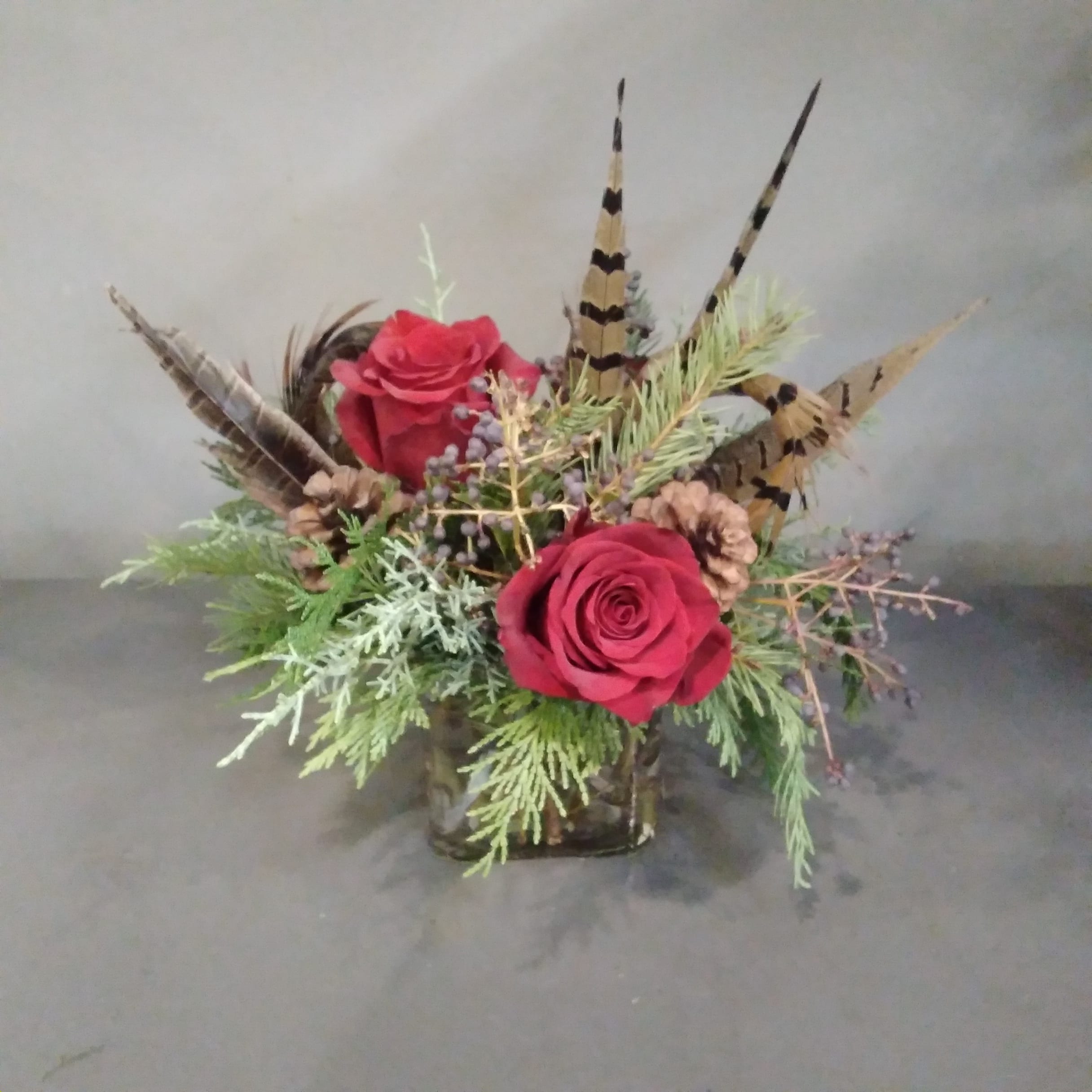 Rustic Winter Cube - A simple, natural design for the minimalistic in your life.  Evergreens, pine cones and pheasant feathers are accented with red roses.  Measures approx. 8x8