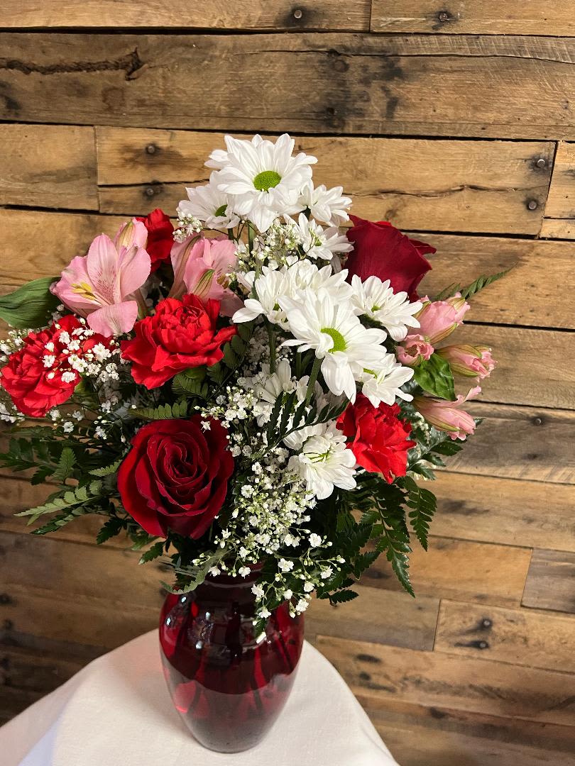 CUTE CUPID - RED VASE FILLED WITH A MIX OF BEAUTIFUL FLOWERS. WILL HAVE ROSES, CARNATIONS, FILLER, ALSTROEMERIA. COLORS MAY VARY