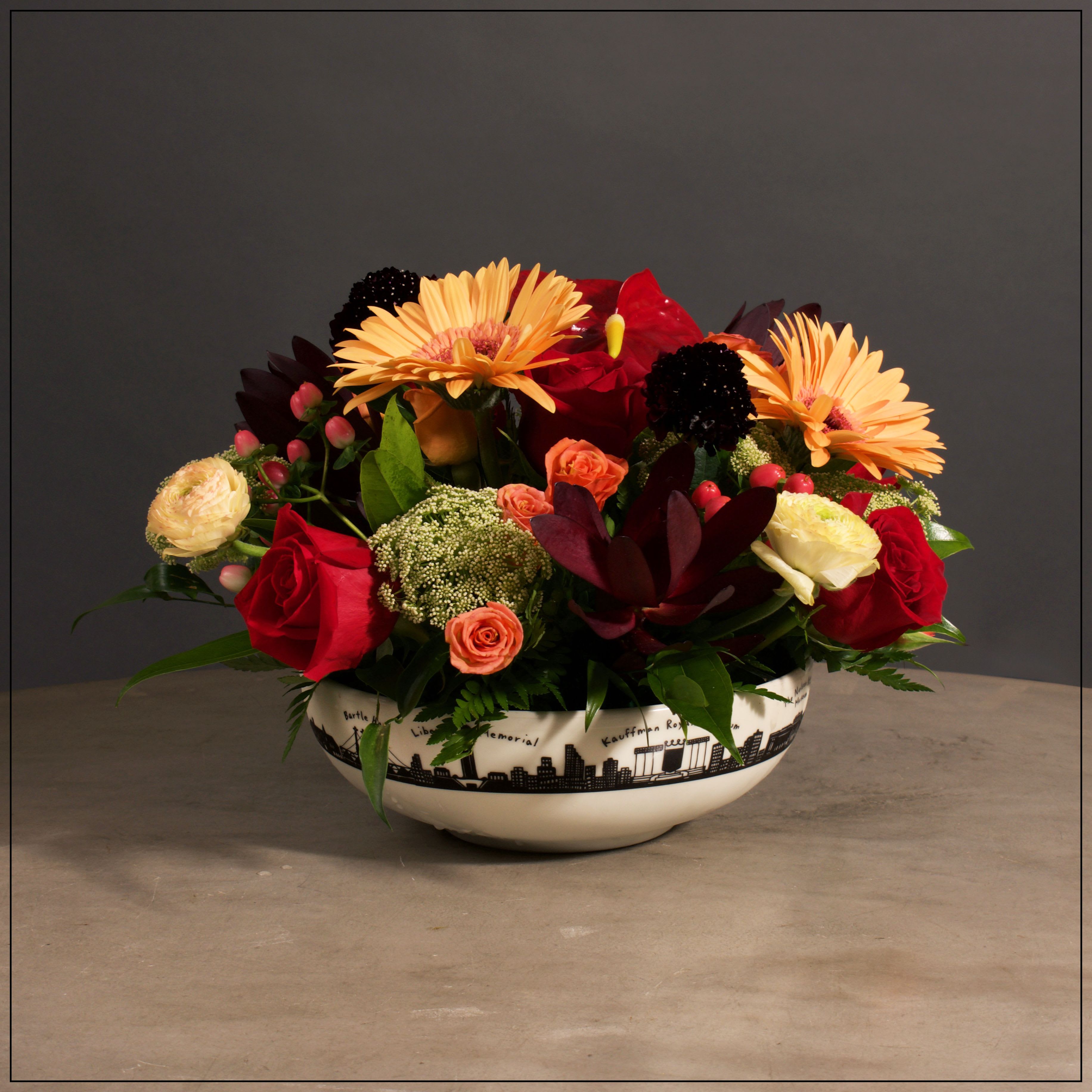 Celebrate KC Center - Our exclusive Kansas City Skyline bowl filled with a beautiful mix of anthurium, roses, spray roses, gerbera daisies, safari sunset protea, ranunculus, scabiosa, and Ammi Majus. Approximate size, 10" tall and 15" wide.