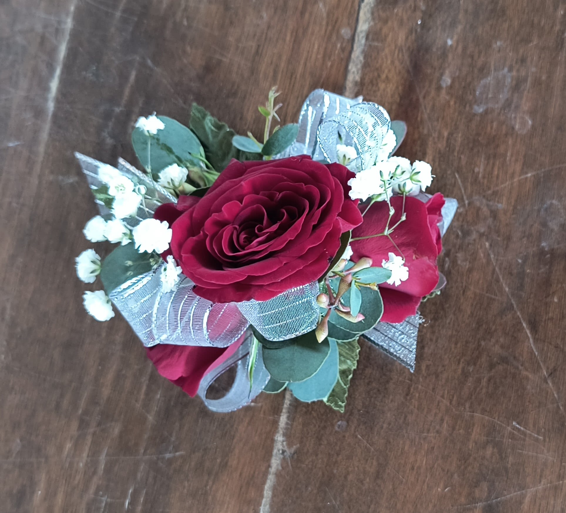 Rouge Wrist Corsage - Classic red roses fresh eucalyptus greens and baby's breath wrist corsage with spray roses accented with silver ribbon. Corsage includes an elastic disposable wristlet.