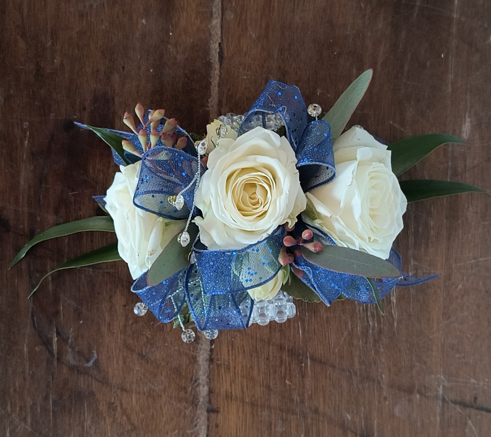 Deluxe Royal Wrist Corsage - Pure white spray rose and royal blue ribbon make this wrist corsage fit for royalty, with fresh greens and gems this wrist corsage has a finished look. Includes a keepsake beaded or pearl wristlet.