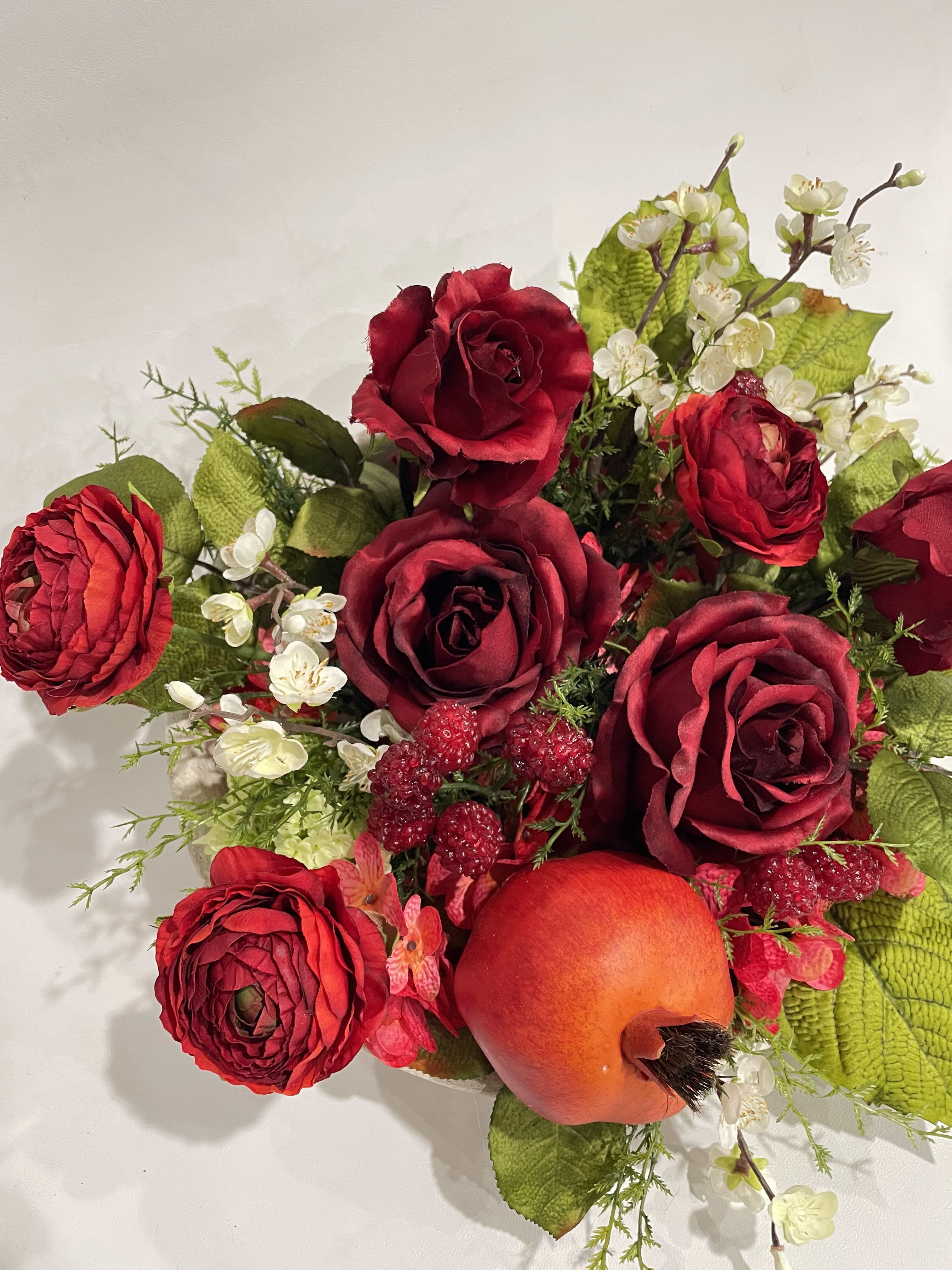 SILK-Winter Warmth Centerpiece - This silk botanical arrangement is designed in a 10" stoneware bowl, making the total design roughly 14" across. Featuring high quality silk blossoms and greenery such as red roses, ranunculus, coral hydrangea, rich leaves, pomegranates, raspberries, and blooming branch snips, this design invokes the rich warmth of winter with hints of the promise of spring.  This is NOT a fresh flower arrangement! This is a permanent silk piece. 