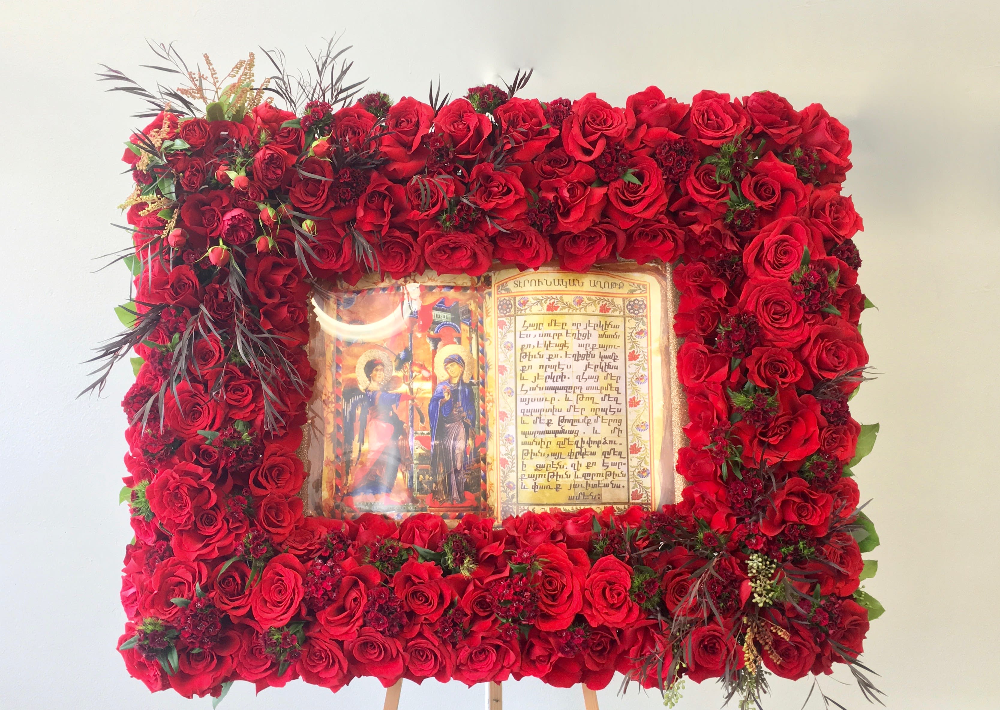 Red Bible Frame  - This frame includes a mix of roses and seasonal greens. Frames are approximately 32 inches wide. Bible is included.     We include easel, printed banner, and delivery (some fees may apply). An additional banner can be added for $15.   