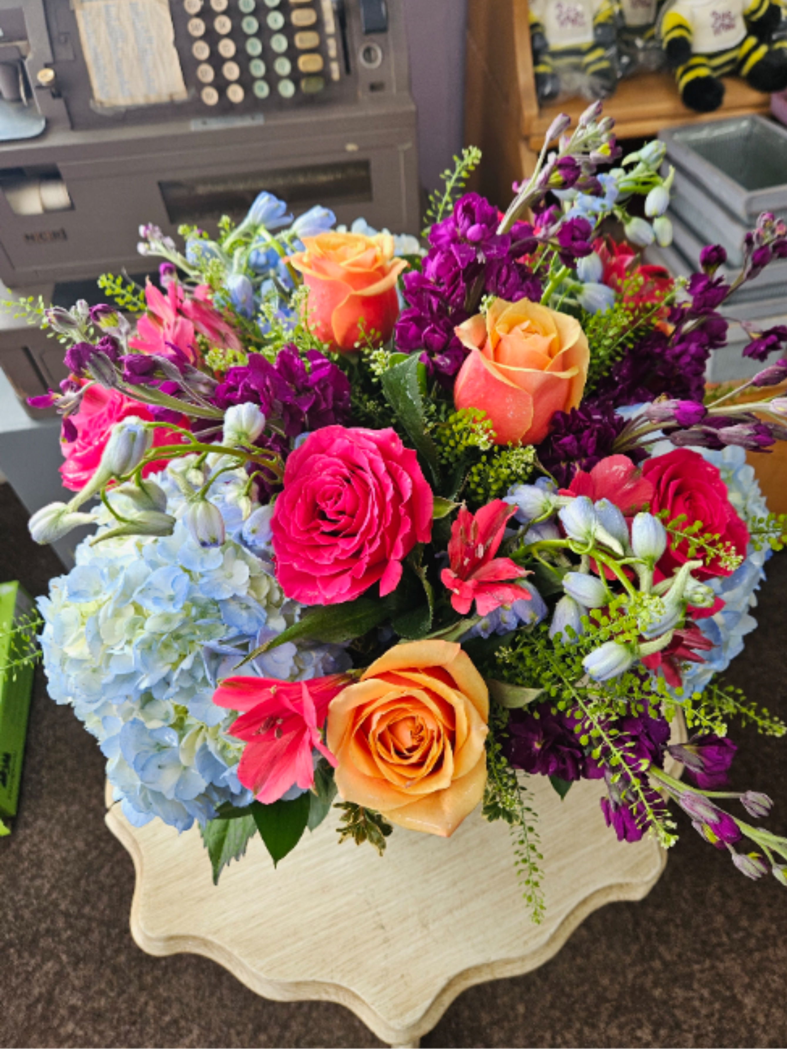 Lavish Birthday Bowl - Stunning mix of pale blue hydrangeas, sky blue delphinium, hot pink and cherry brandy roses, purple stock and an ever changing mix of other flowers make this a stunning birthday gift arranged in a leaf lined 8” bubble bowl. 