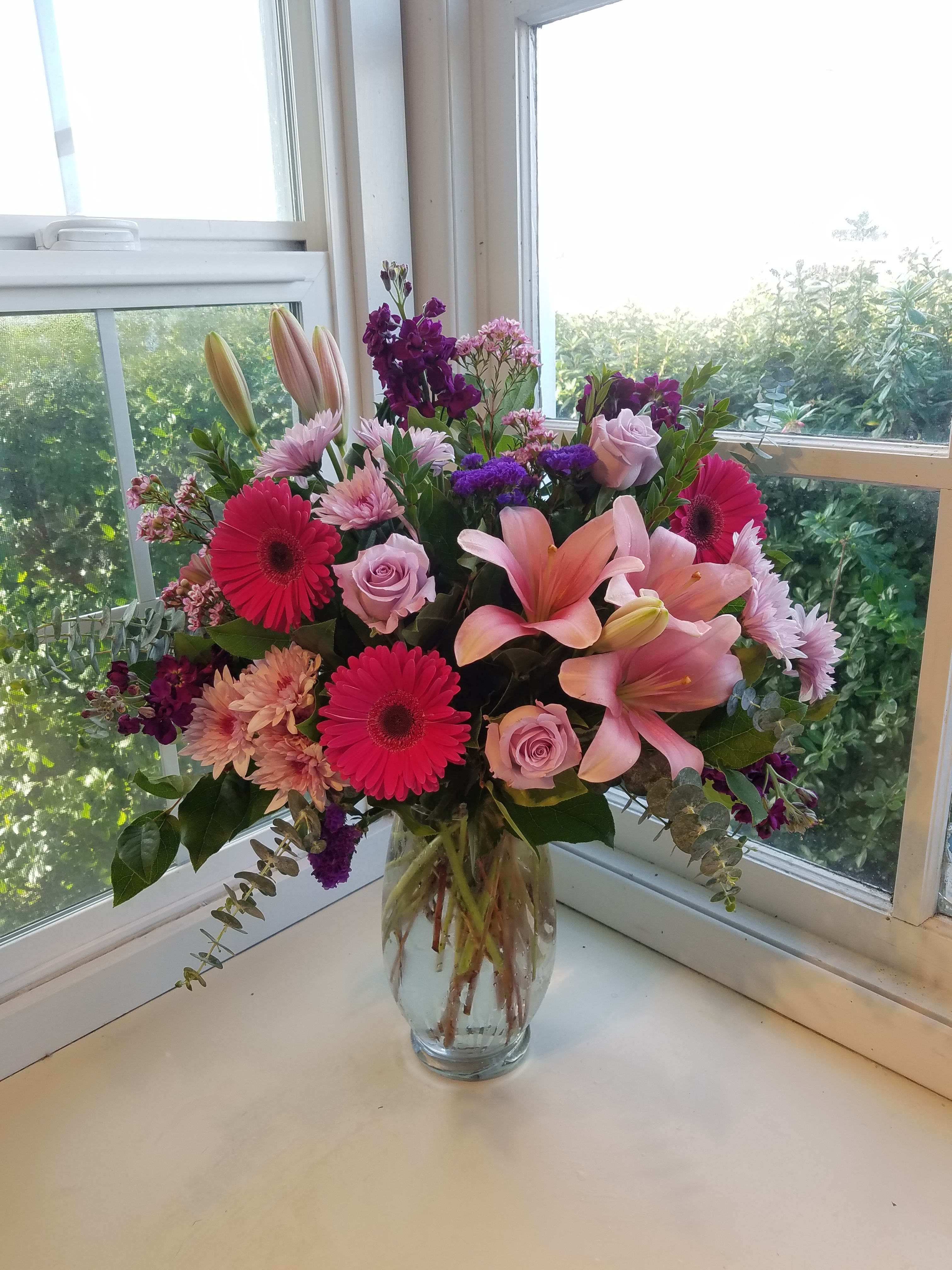 Raspberry Beret - Fuscia gerb daisies pop against softer pink and lavender flowers such as lilies, roses and chrysanthemums.  Touches of dark purple add a bit of depth.  As always, flowers and container are subject the substitution based on what we have in stock. 