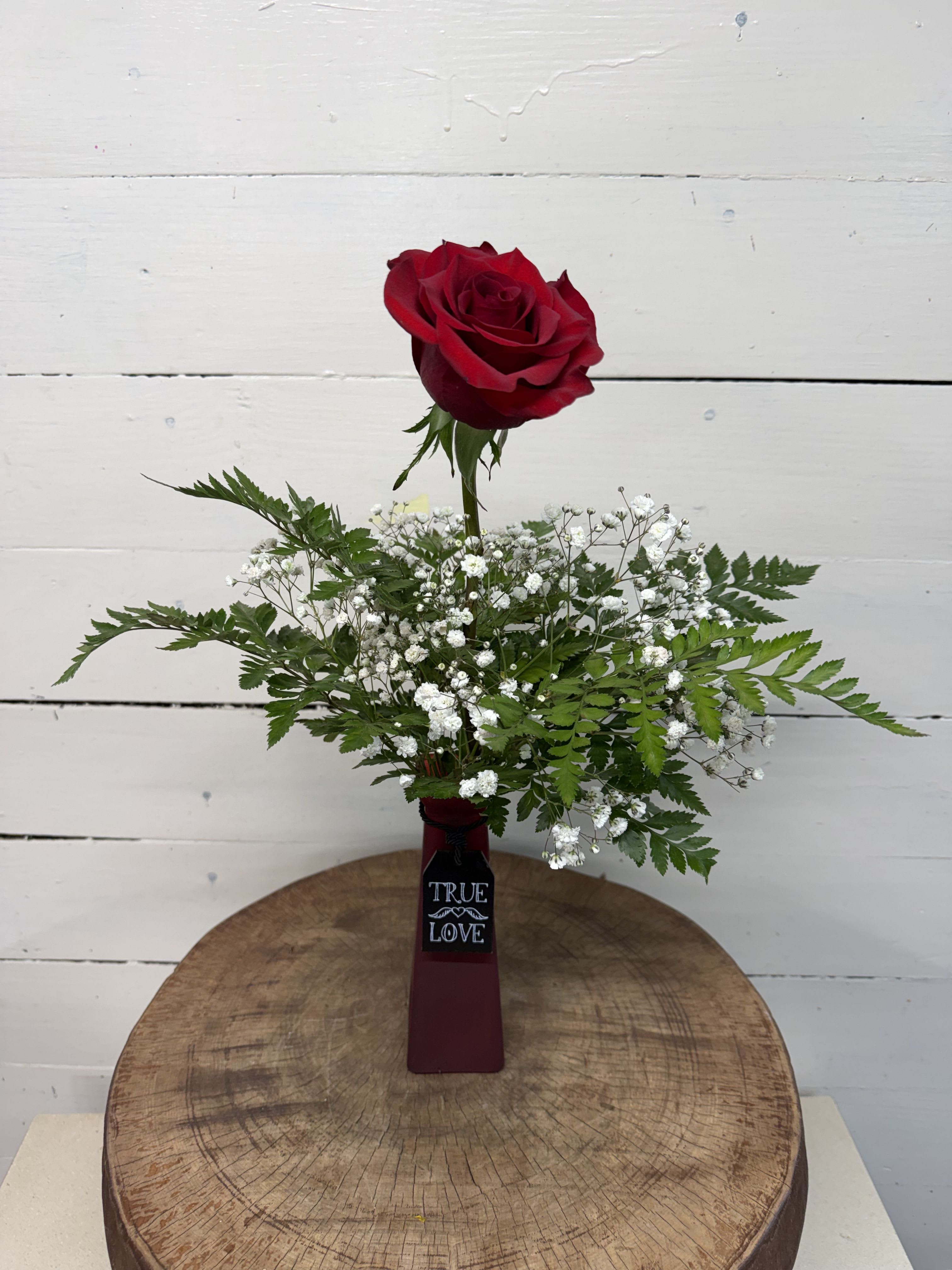 Valentine Bud Vase Collection - Our Valentine bud vase collection, features one of our highest quality roses surrounded by baby's breath and greenery making it the perfect token of elegance and romance.  The red bud vase will feature a red rose. The pink vase will feature a hot pink rose. The frosted vase will feature a peach rose. Please specify your choice of vase color at checkout. Approximately 6" W x 16" H