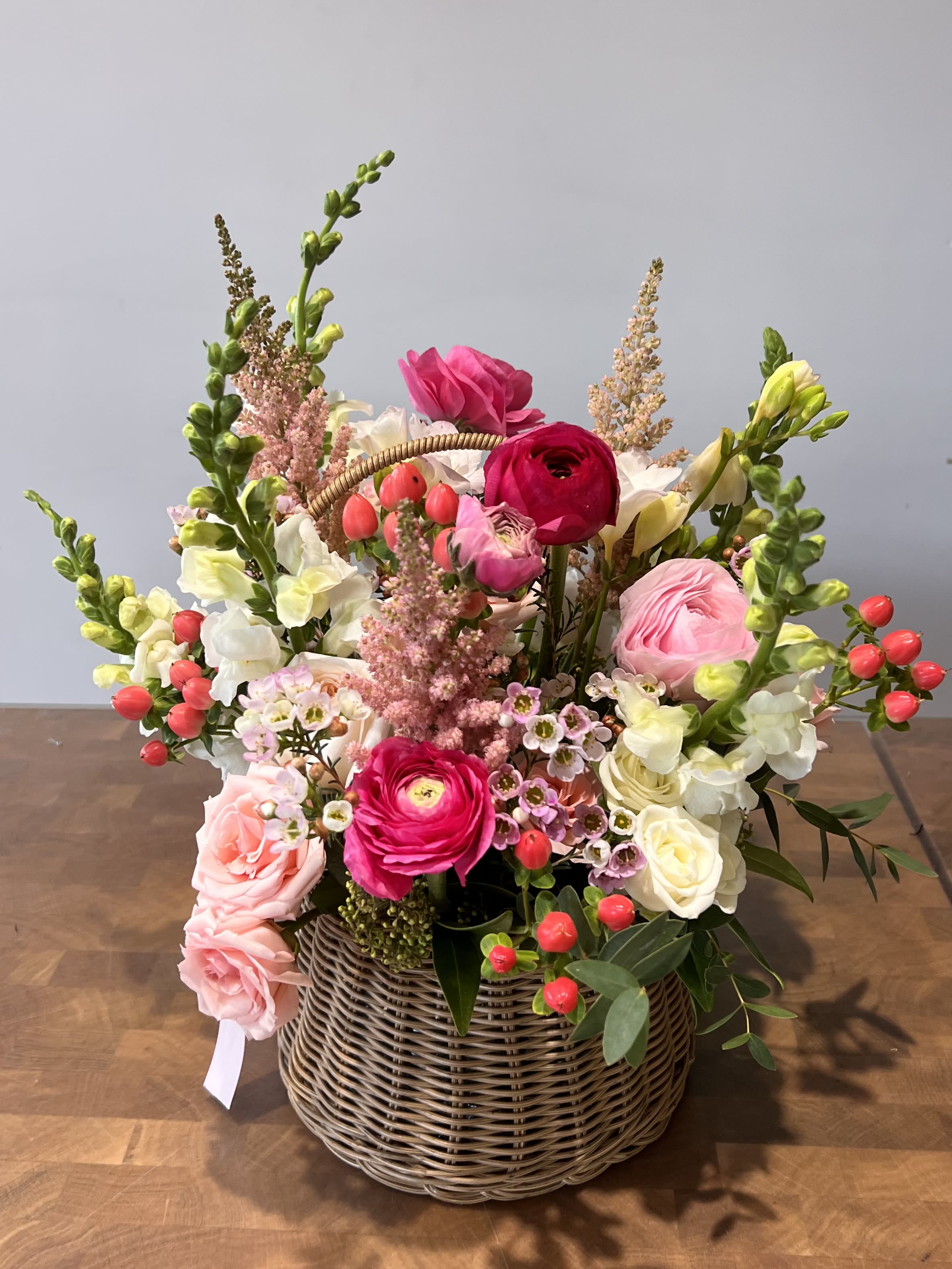 Garden Love  - A timeless and romantic floral arrangement featuring delicate ranunculus, anemones, roses, and lush greenery in a charming woven basket