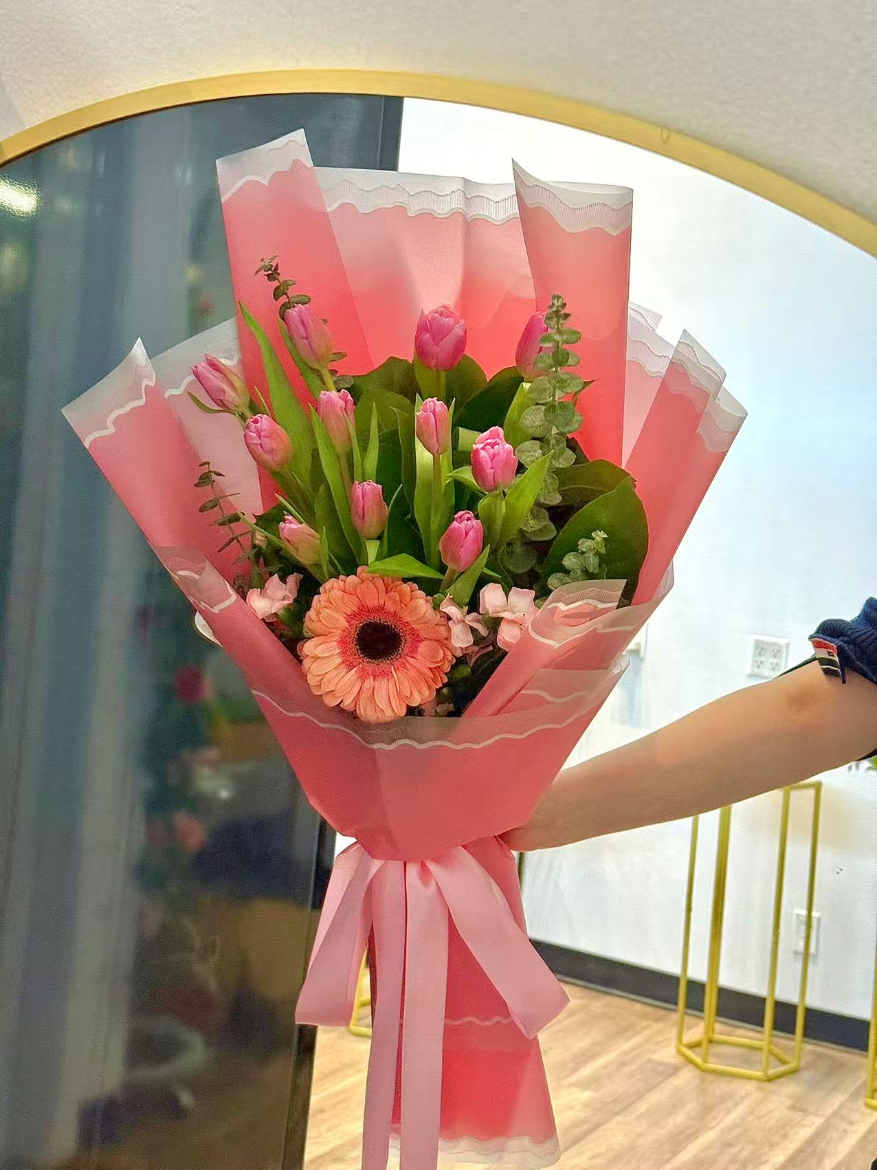 Tulips Lover by Tiffany's Blooms - A soft and cheerful arrangement featuring fresh pink tulips, accented with seasonal blooms and lush greenery. Hand-wrapped in elegant layered paper, this bouquet is perfect for birthdays, thank-you gifts, or everyday moments worth celebrating.  Each bouquet is made fresh to order. Flower varieties may vary slightly based on seasonal availability.