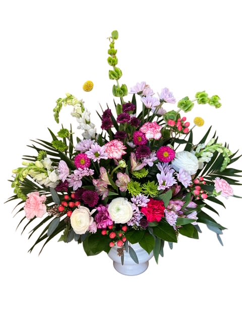 Garden Memories Tribute - A soft and graceful tribute filled with the beauty of a blooming garden. This arrangement features a lovely mix of pinks, purples, and whites with accents of fresh greenery, Bells of Ireland, and cheerful textures. Presented in a white urn, it’s a heartfelt expression of love and remembrance, perfect for honoring a cherished life at a funeral or memorial service.
