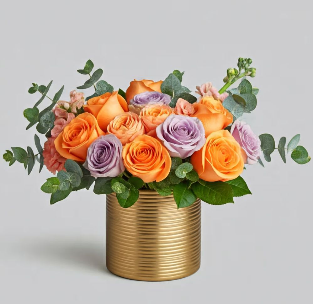 Golden Horizon - The Golden Horizon Arrangement  Celebrate in style with our Golden Horizon arrangement. This stunning design features a modern and sophisticated aesthetic, perfect for making a statement at a special event or as an elegant centerpiece in your home.  This unique display features a vibrant blend of orange and lavender roses, with delicate baby blue eucalyptus adding a touch of whimsy. All of these beautiful blooms are expertly arranged in a sleek gold ceramic vase, creating a striking contrast of color and texture.  Bring a touch of modern elegance into any space. Order the Golden Horizon today and send a gift that's as unique as they are.