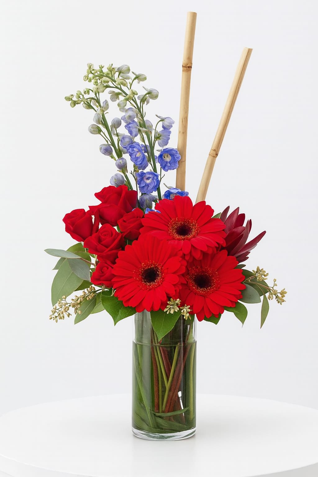 Art In Bloom - A artful display of Gerbera Daisies with Delphinium, Roses, exotic foliage's, and finished off with a display of sugar cane.  Perfect for an office setting or a gift for a person with a modern lifestyle.