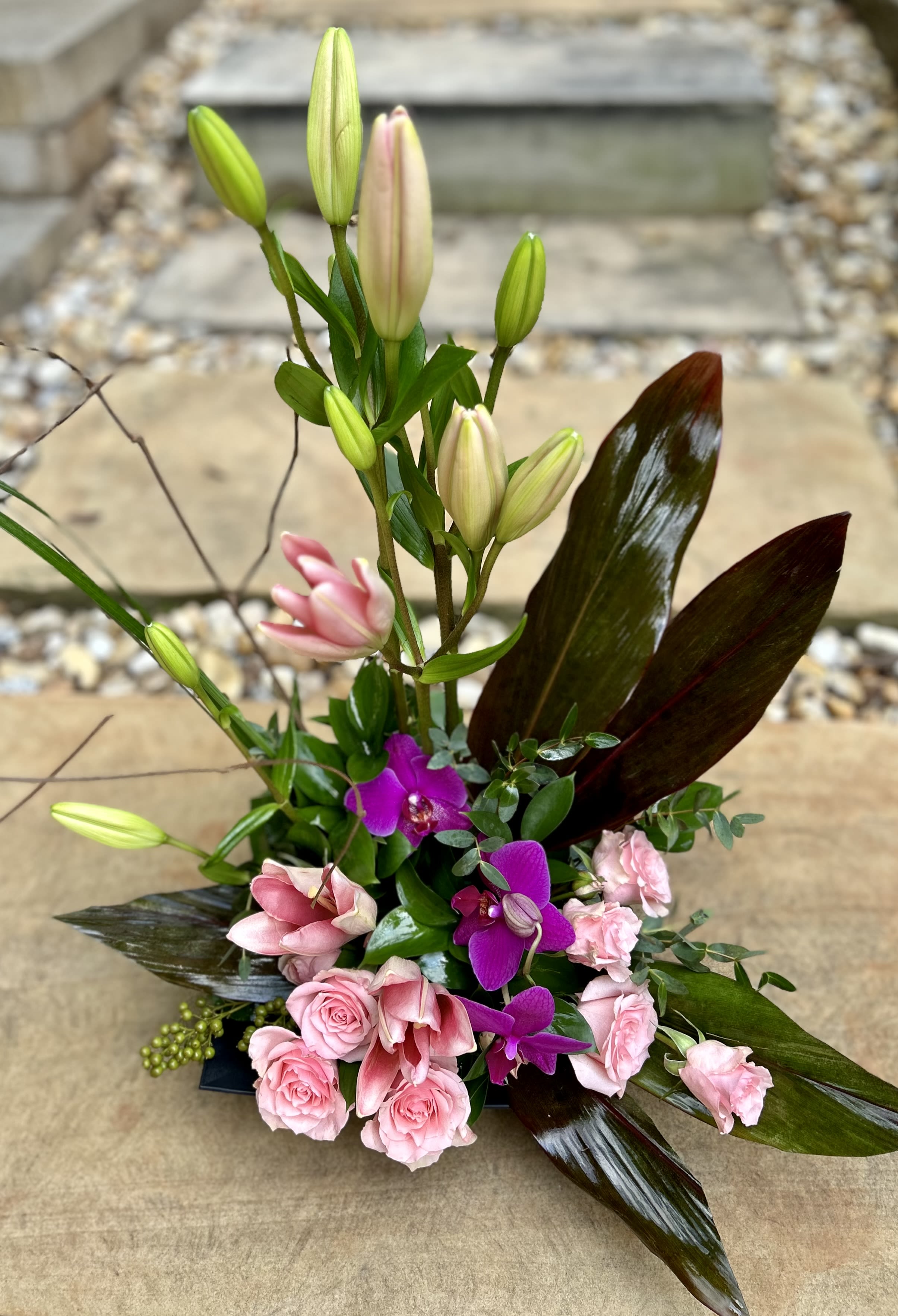Pink Tropics - Pink lilies, purple orchids and spray roses with beautiful leaves arranged in a modern style.